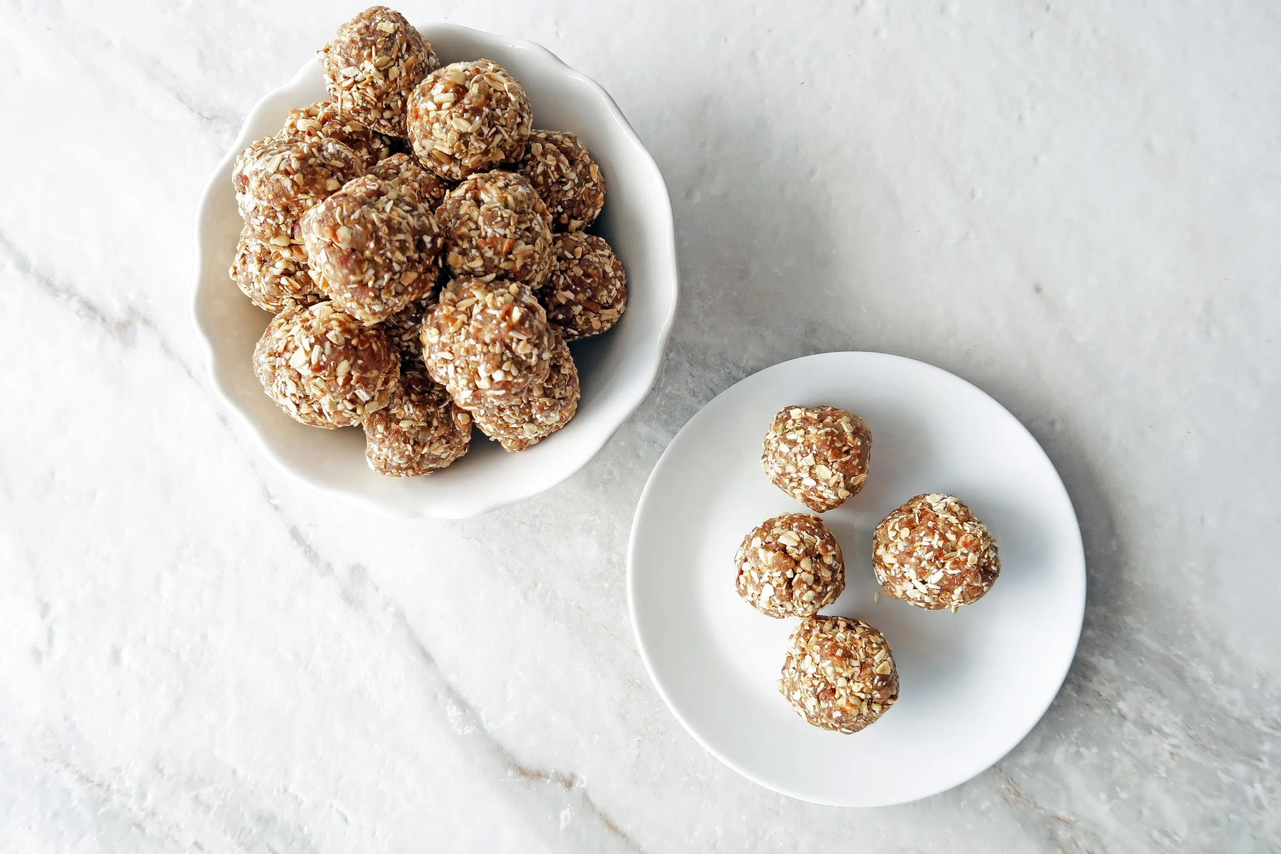 No Bake Chai Spiced Date Energy Balls piled in a white bowl with four energy balls on a white plate to its side.
