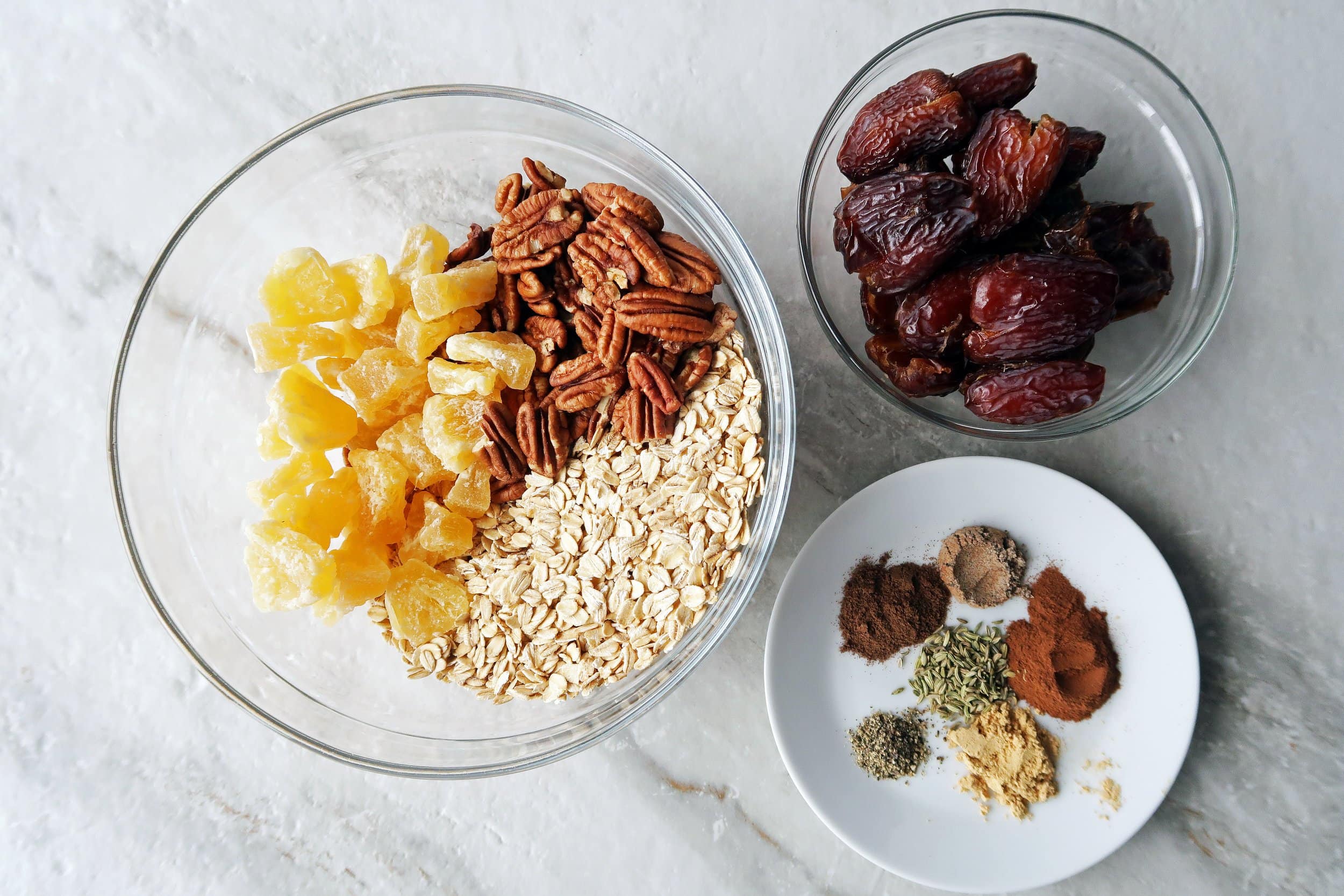 Bowls filled with dried dates, rolled oats, dried peaches, pecans, and chai spices.