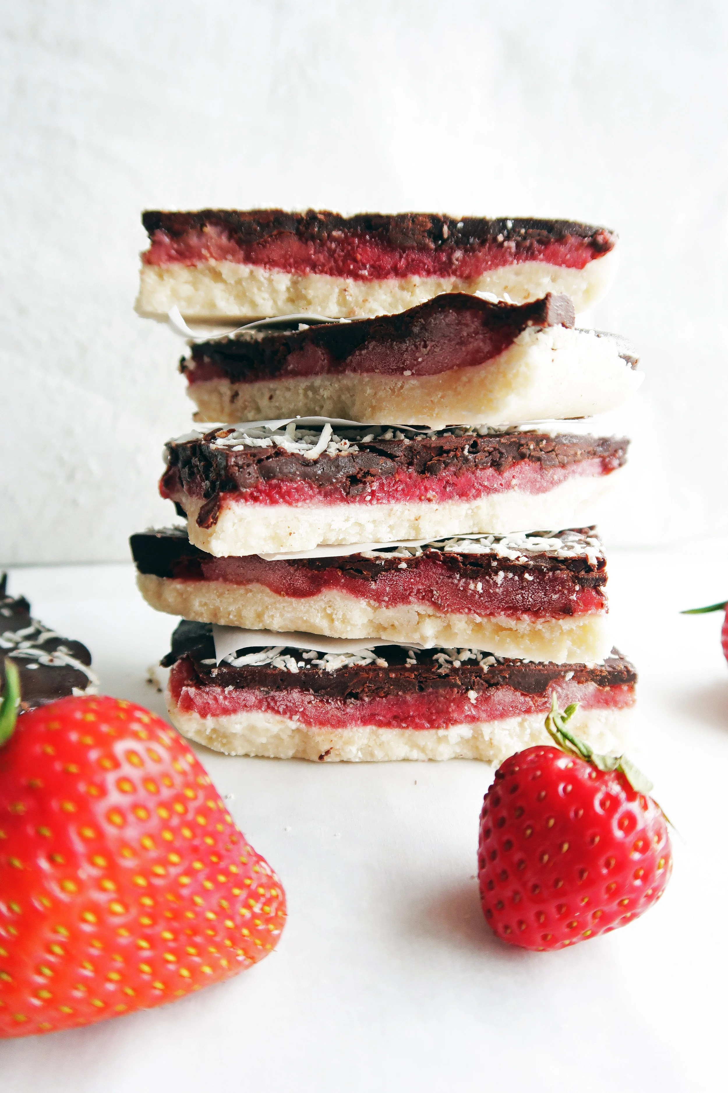 Five No-Bake Chocolate Strawberry Coconut Bars placed on top of one another with strawberries around the bars.  