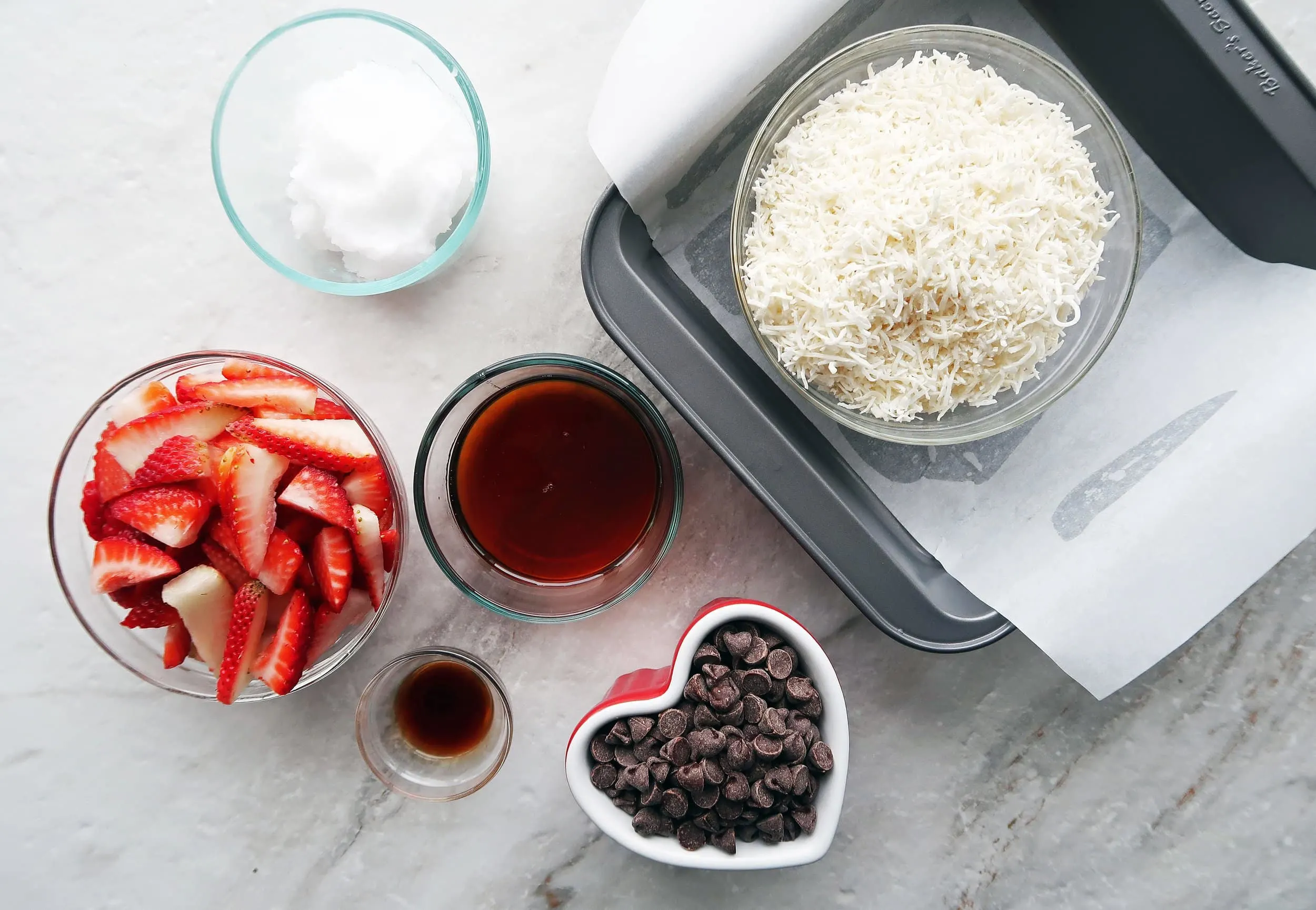 Bowls of strawberries, chocolate chips, maple syrup,and shredded coconut.