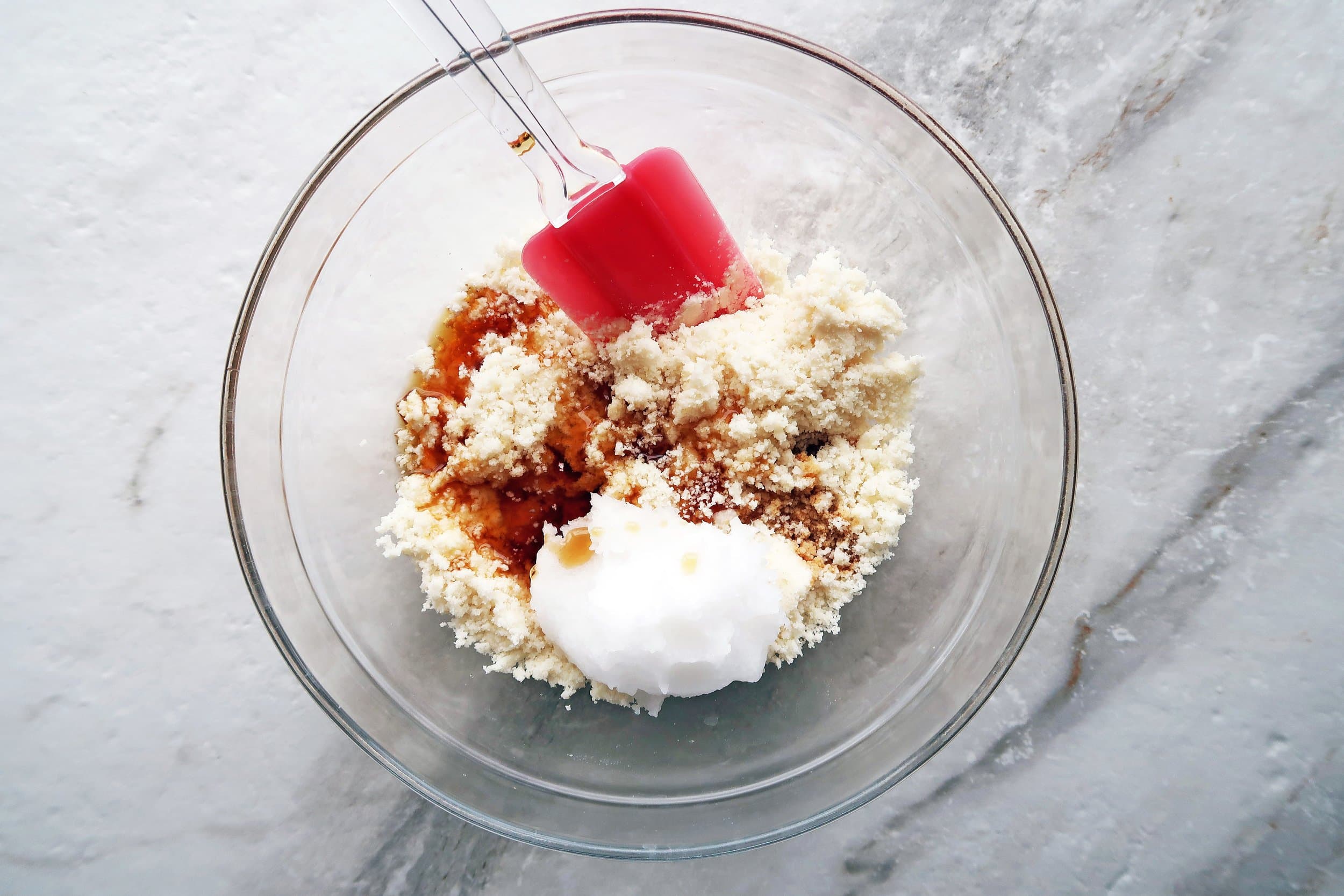 Shredded coconut in a bowl with coconut oil, maple syrup, and vanilla.