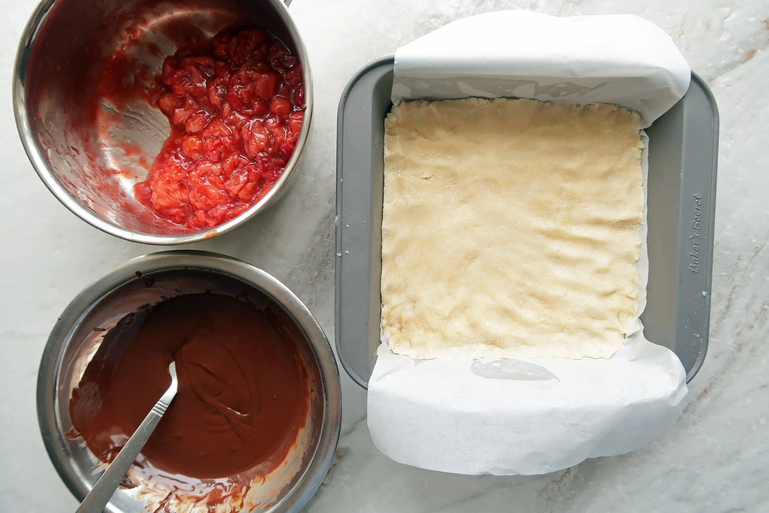 A pan of coconut next to a bowls of melted chocolate and mashed strawberries.