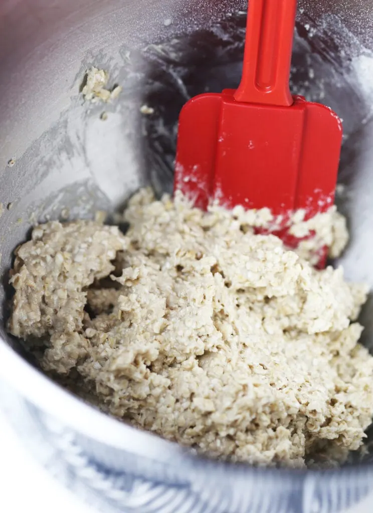 Raw oatmeal cookie dough in a large stainless steel bowl with a red spatula in it.