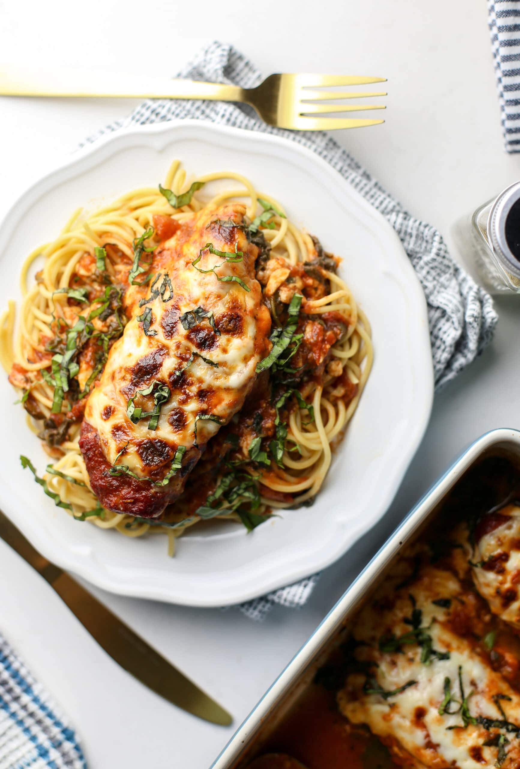 Overhead view of a white plate containing spaghetti topped with baked mozzarella chicken with marinara sauce.