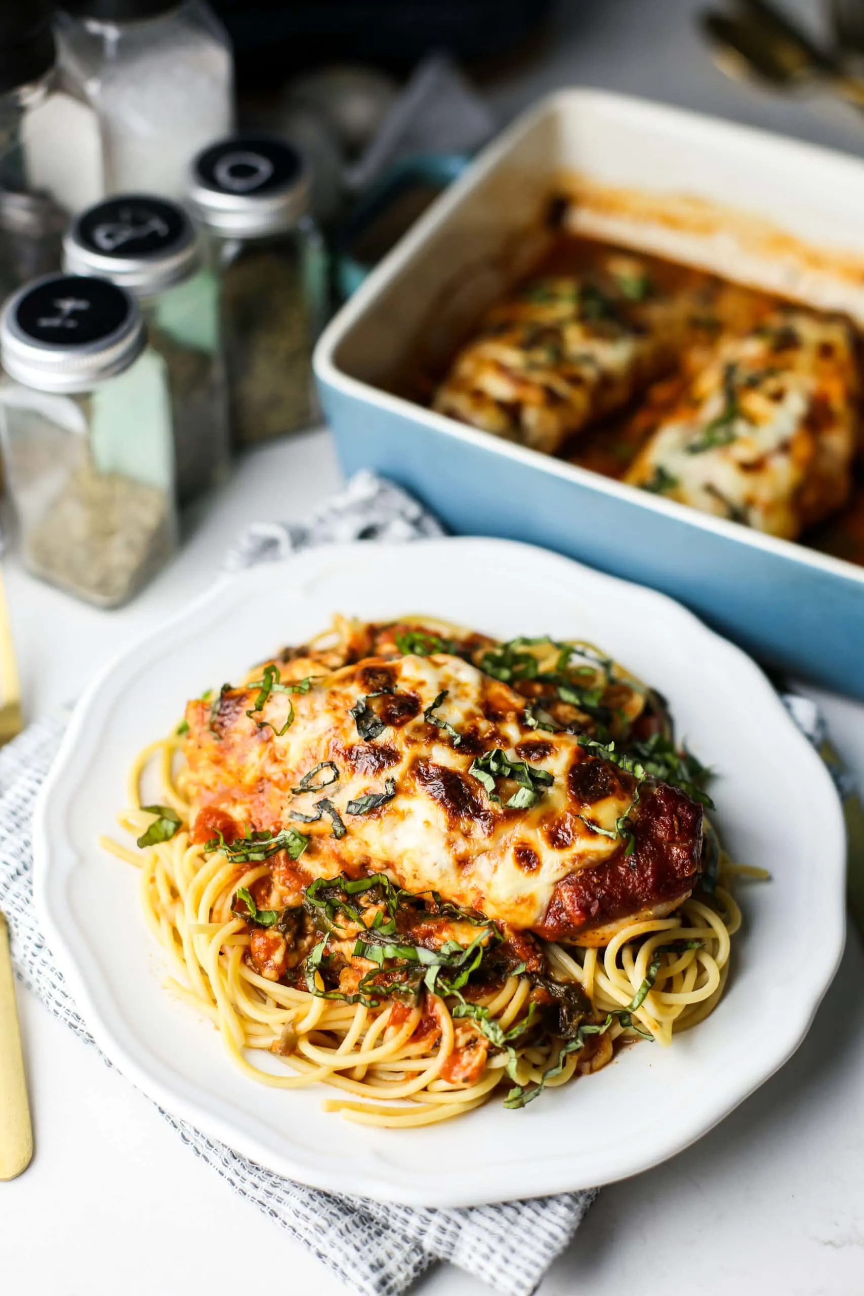 A top angled view of mozzarella chicken with marinara sauce on top of spaghetti on a white plate.