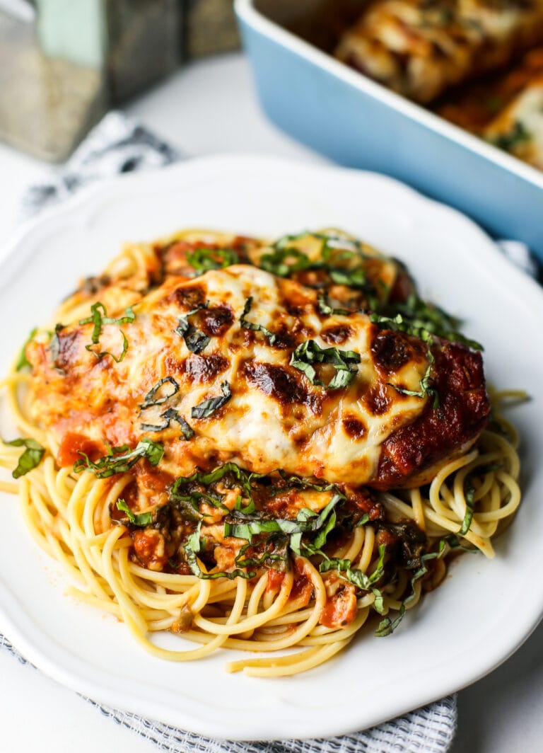 A close-up view of mozzarella chicken with marinara sauce and spaghetti on a white plate.