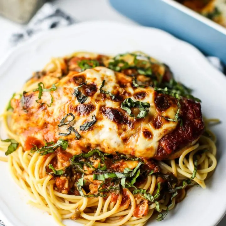 A close-up view of mozzarella chicken with marinara sauce and spaghetti on a white plate.