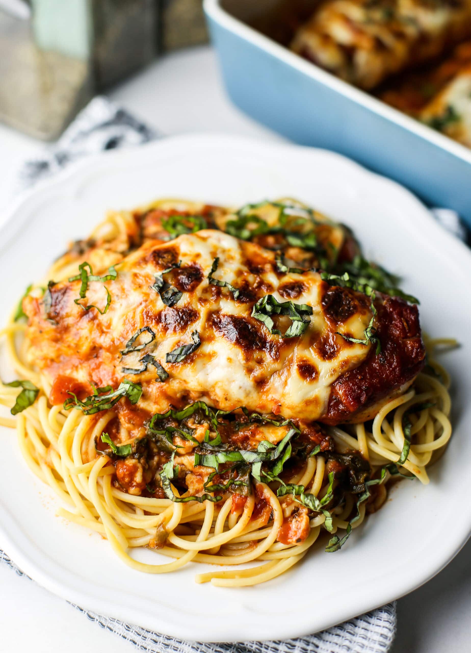 A close-up view of mozzarella chicken with marinara sauce and spaghetti on a white plate.