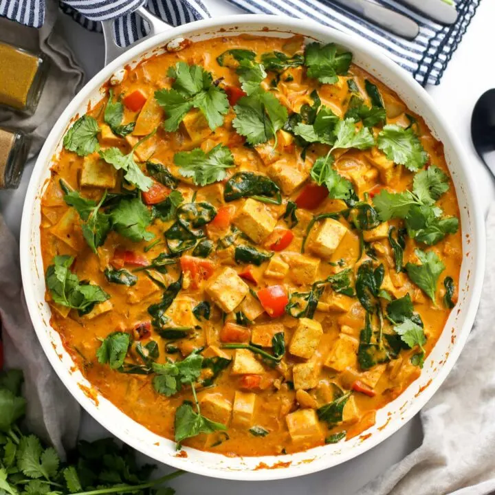 Overhead view of creamy and colourful tofu coconut curry in a large white skillet.