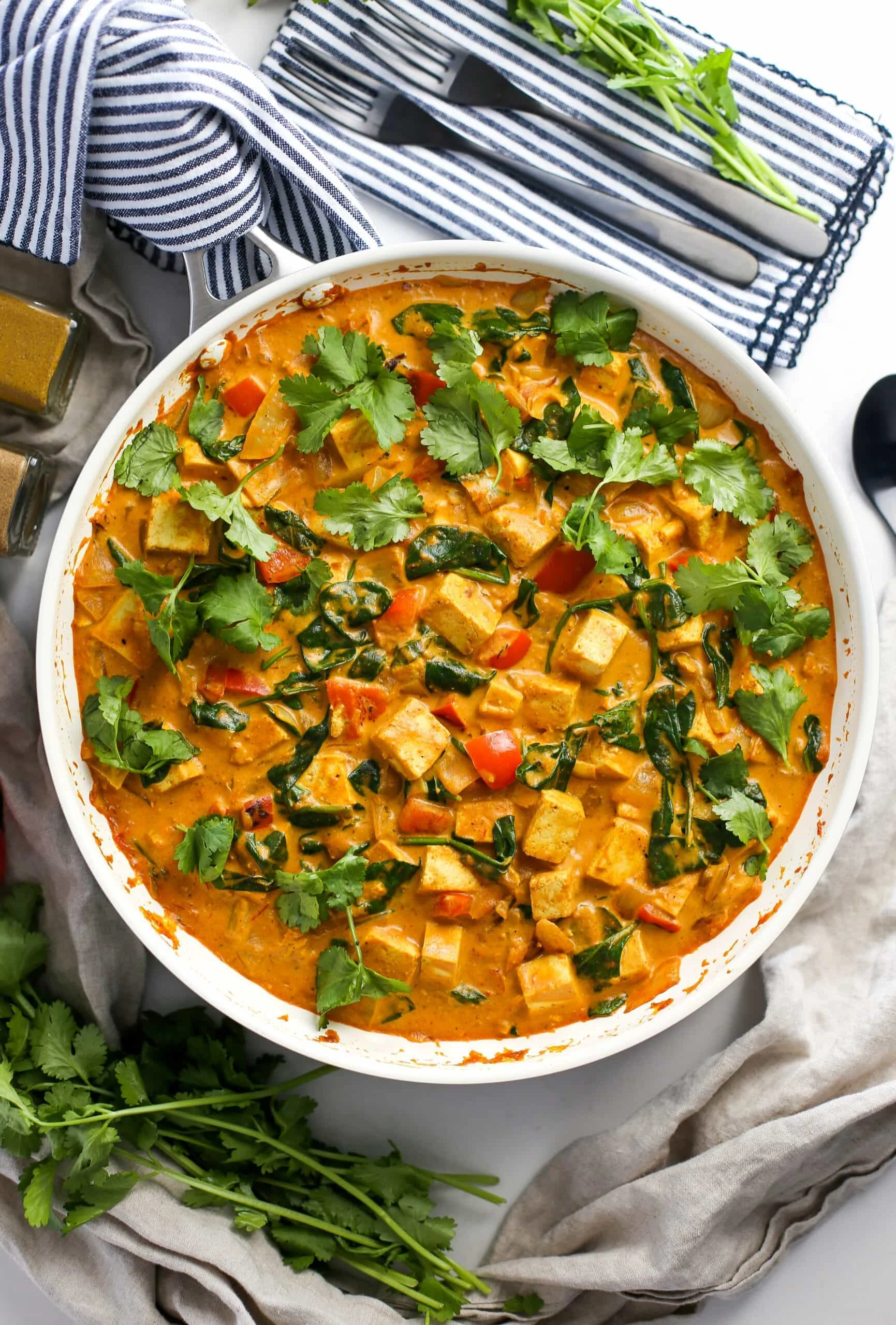 Overhead view of creamy and colourful tofu coconut curry in a large white skillet.