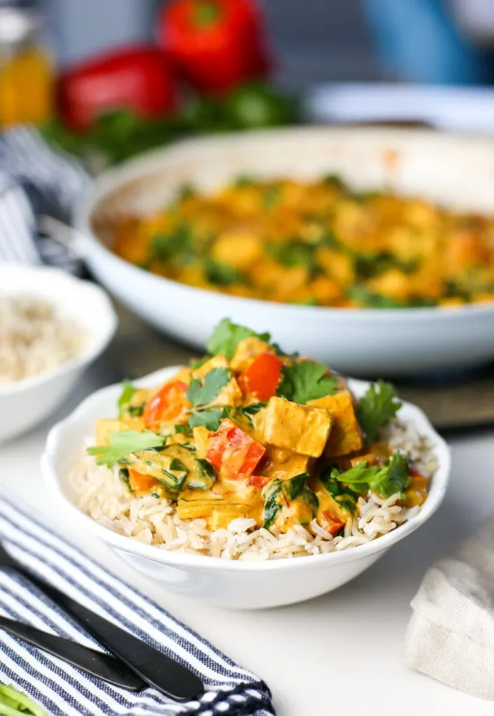 Creamy tofu coconut curry with brown rice in a white bowl.