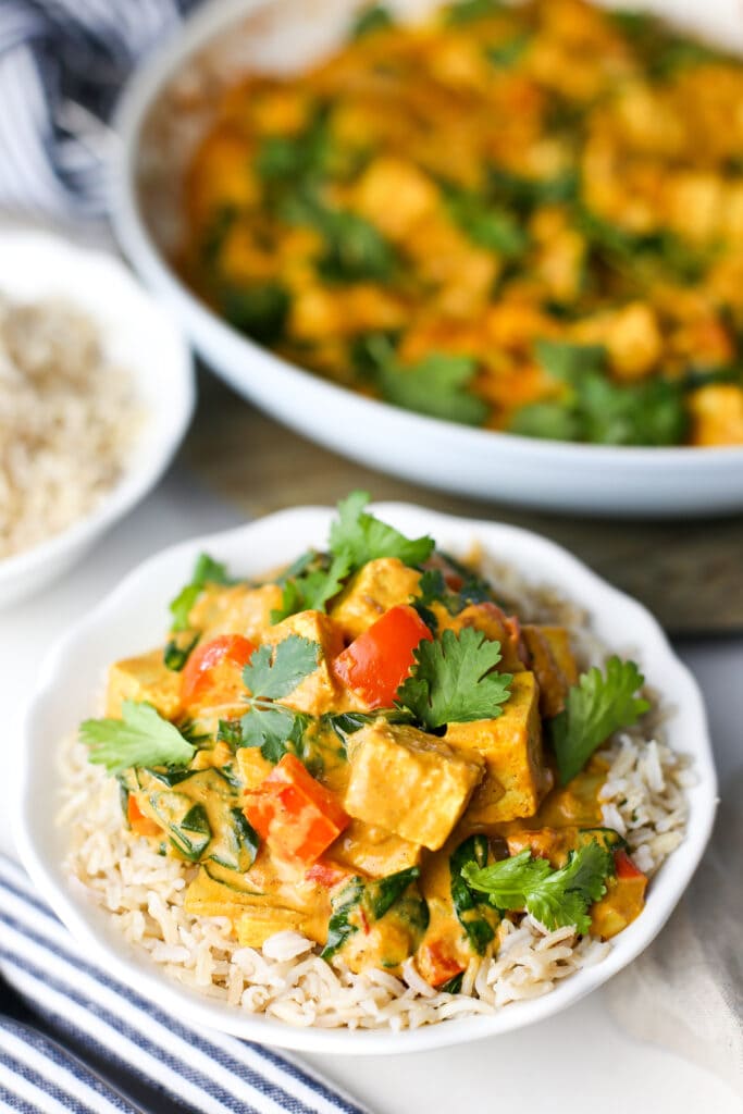 Delicious tofu coconut curry with fresh cilantro on top of brown rice in a white bowl.