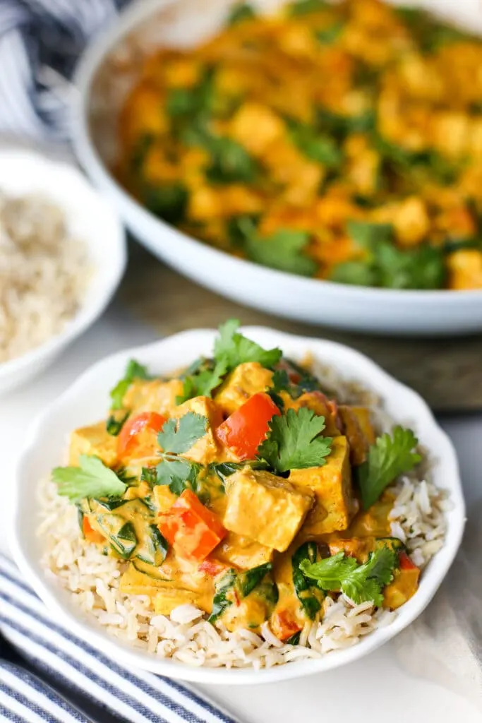 Delicious tofu coconut curry with fresh cilantro on top of brown rice in a white bowl.