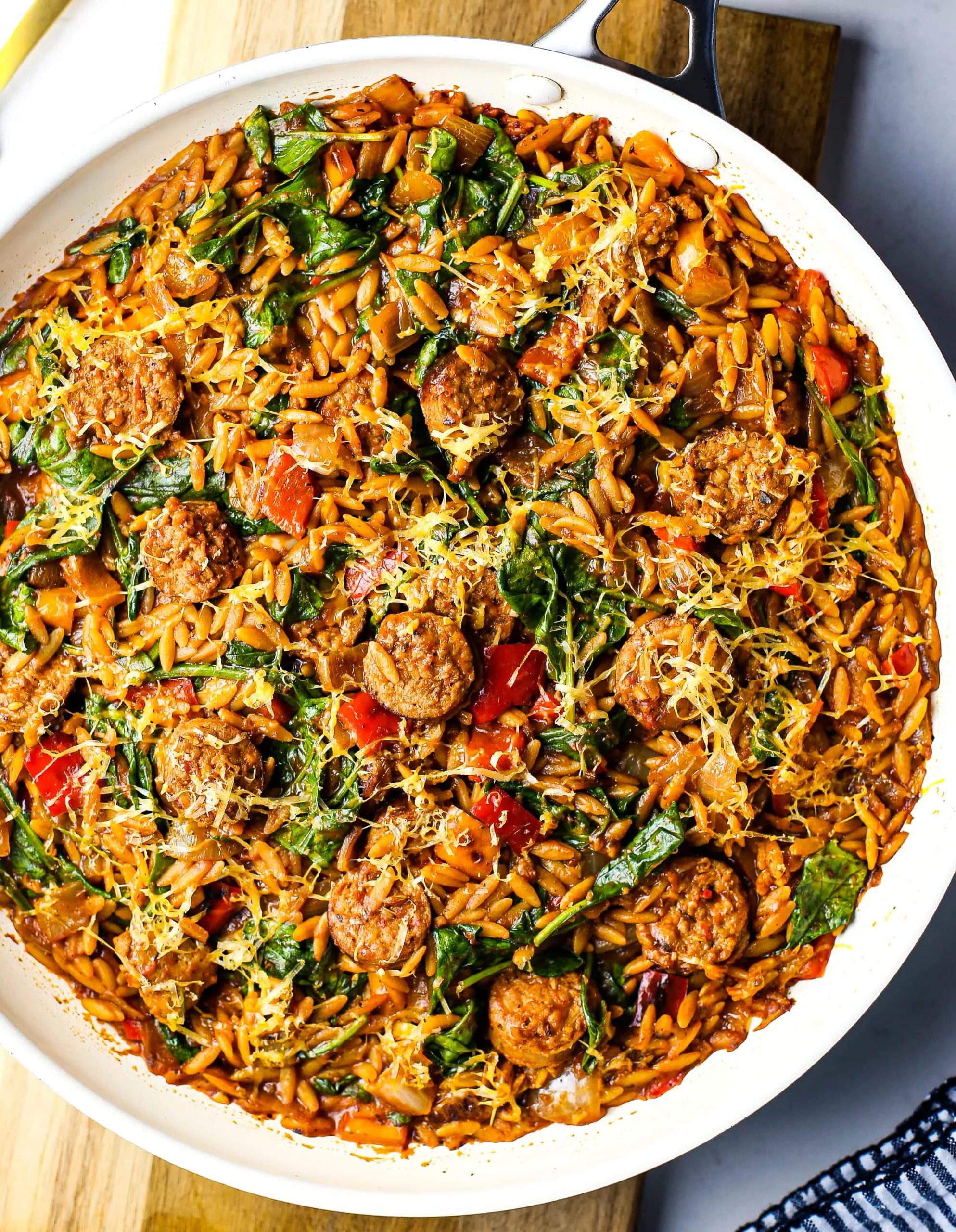 Overhead shot of a frying pan containing sliced Italian sausage, orzo pasta, and vegetables in a marinara sauce.