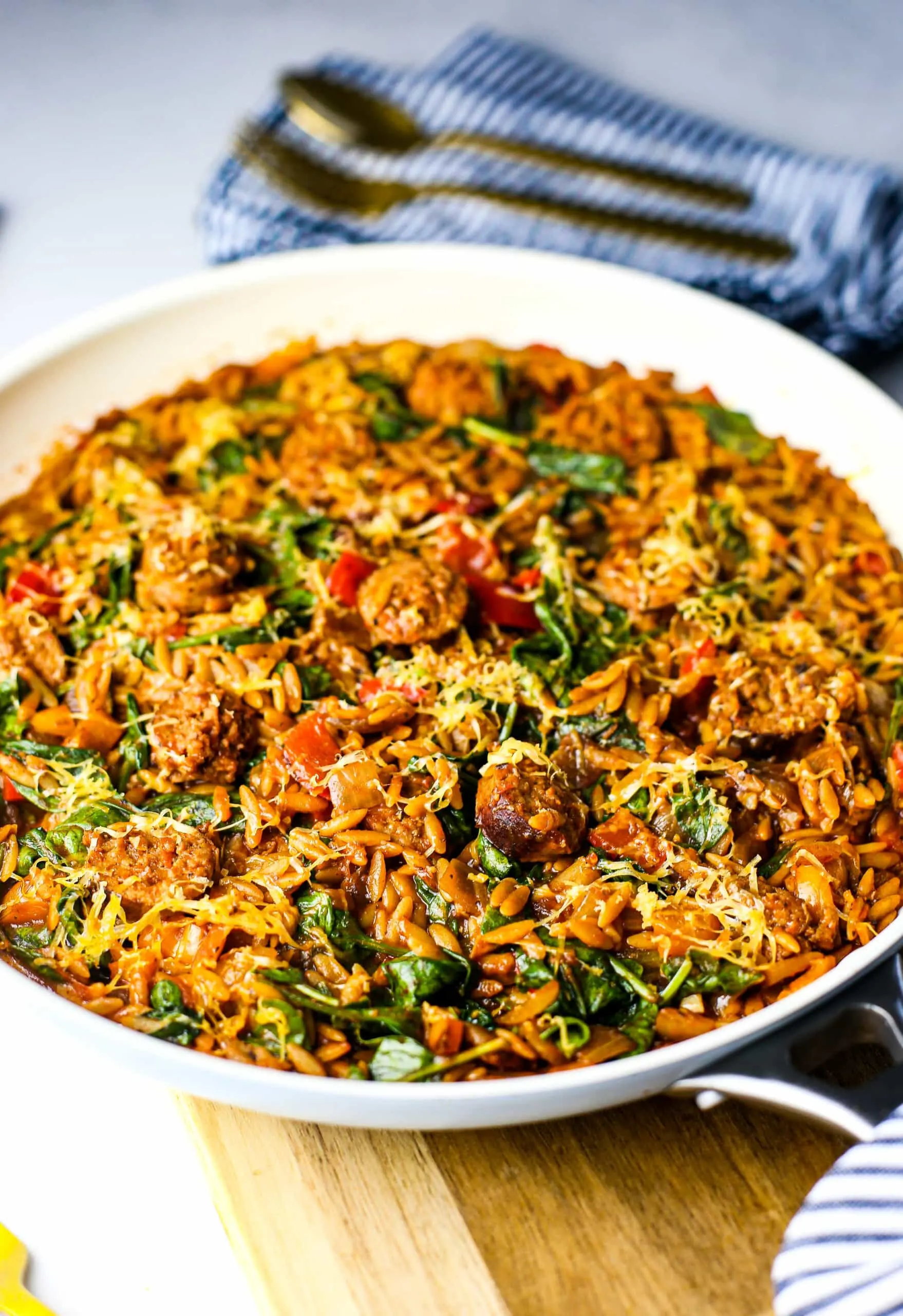 A top-angled view of a white frying pan full of orzo pasta with Italian sausage, onions, and peppers in a marinara sauce.