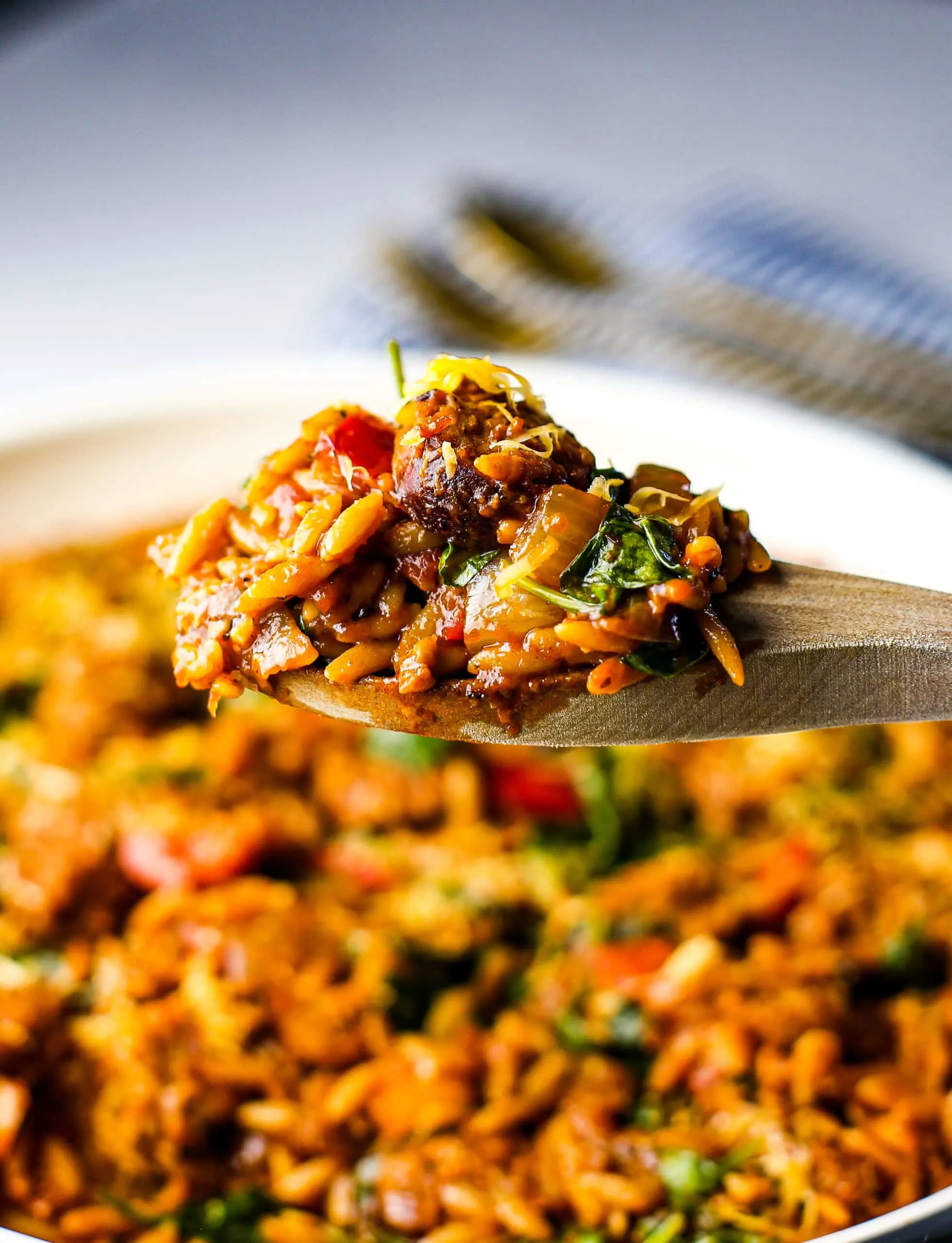 A closeup side view of wooden spoon holding Italian sausage slices, vegetables, and orzo pasta.