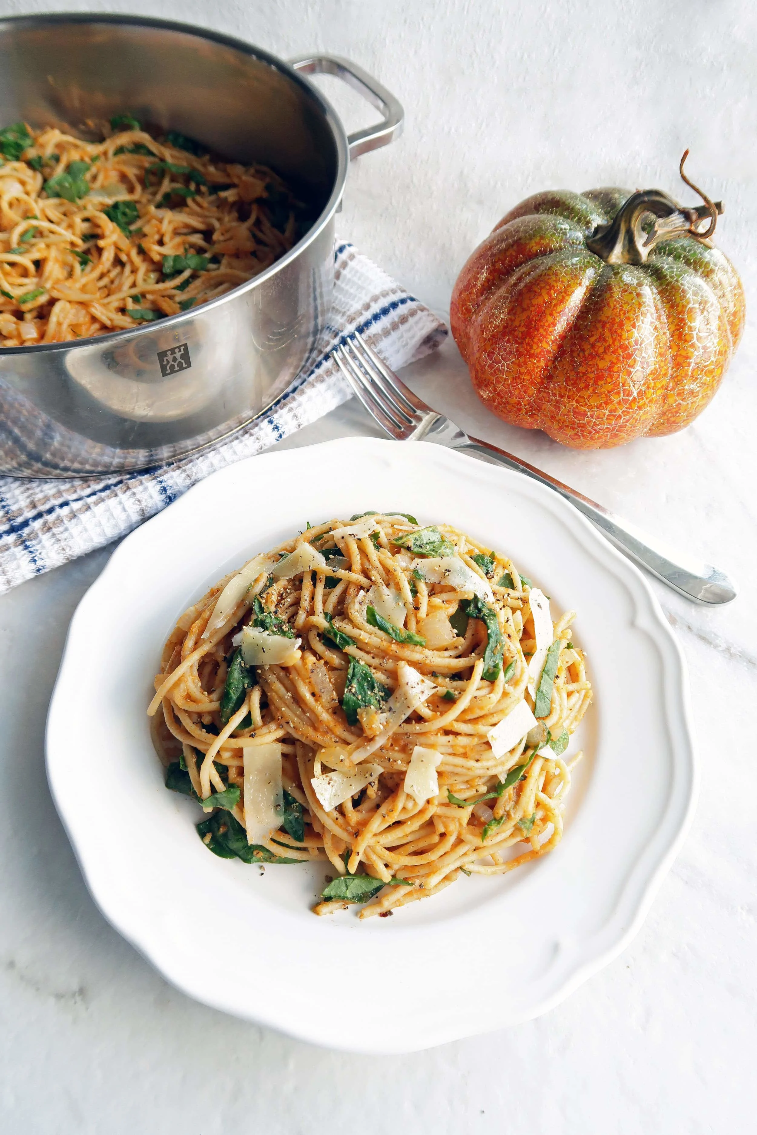 Spaghetti with creamy pumpkin sauce on white plate with more spaghetti in a metal pot in the background.