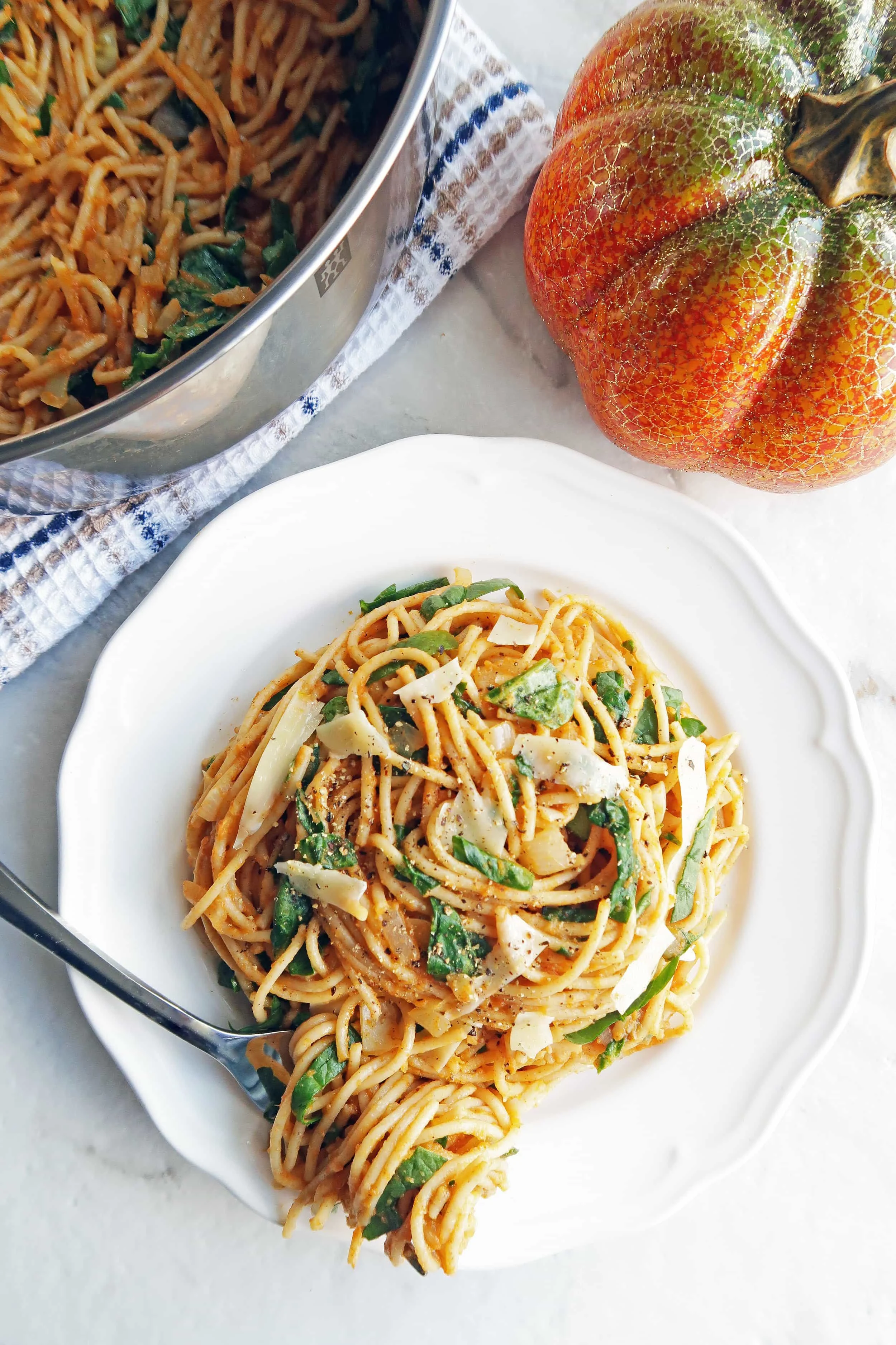 Spaghetti with creamy pumpkin sauce on white plate with more spaghetti in a metal pot behind the plate.