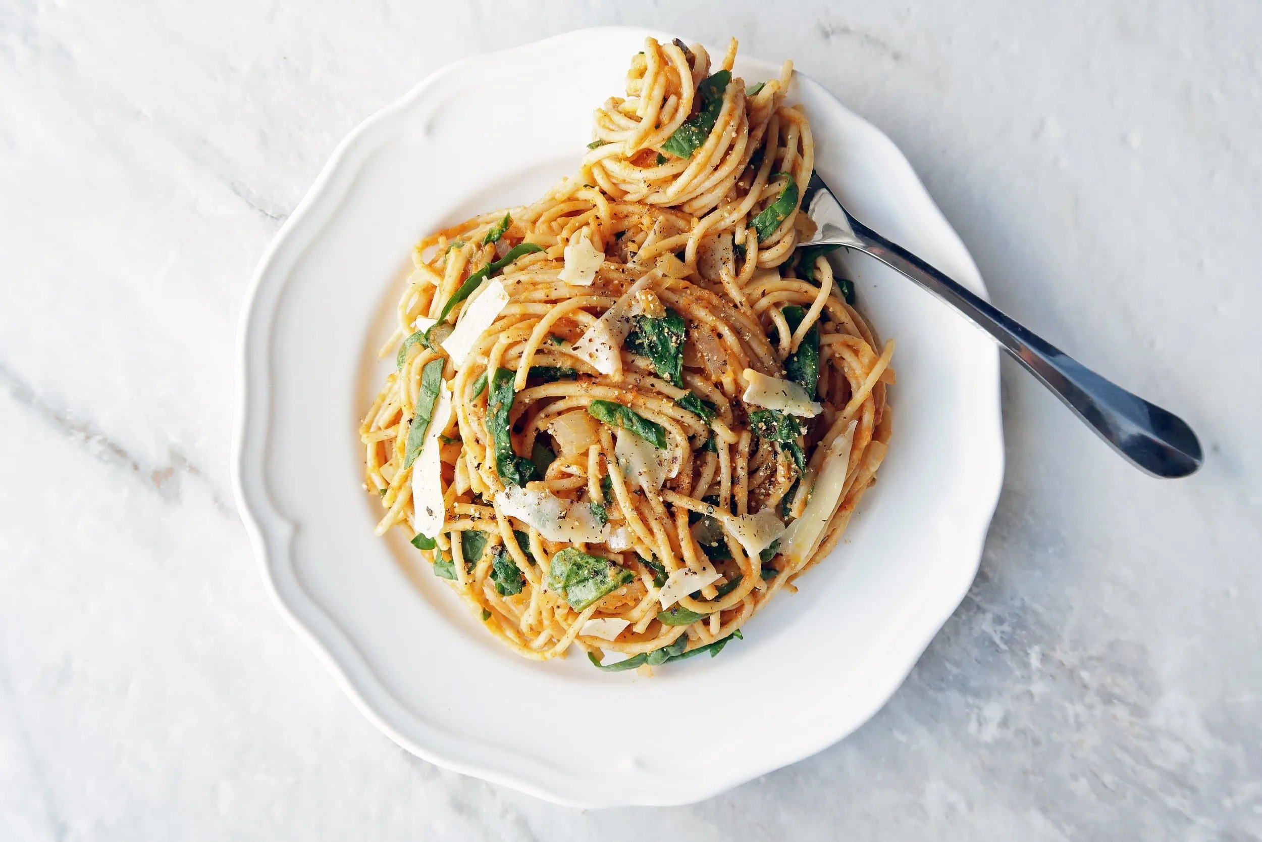 Overhead view of spaghetti with creamy pumpkin sauce on a white plate with spaghetti twirled around a folk.