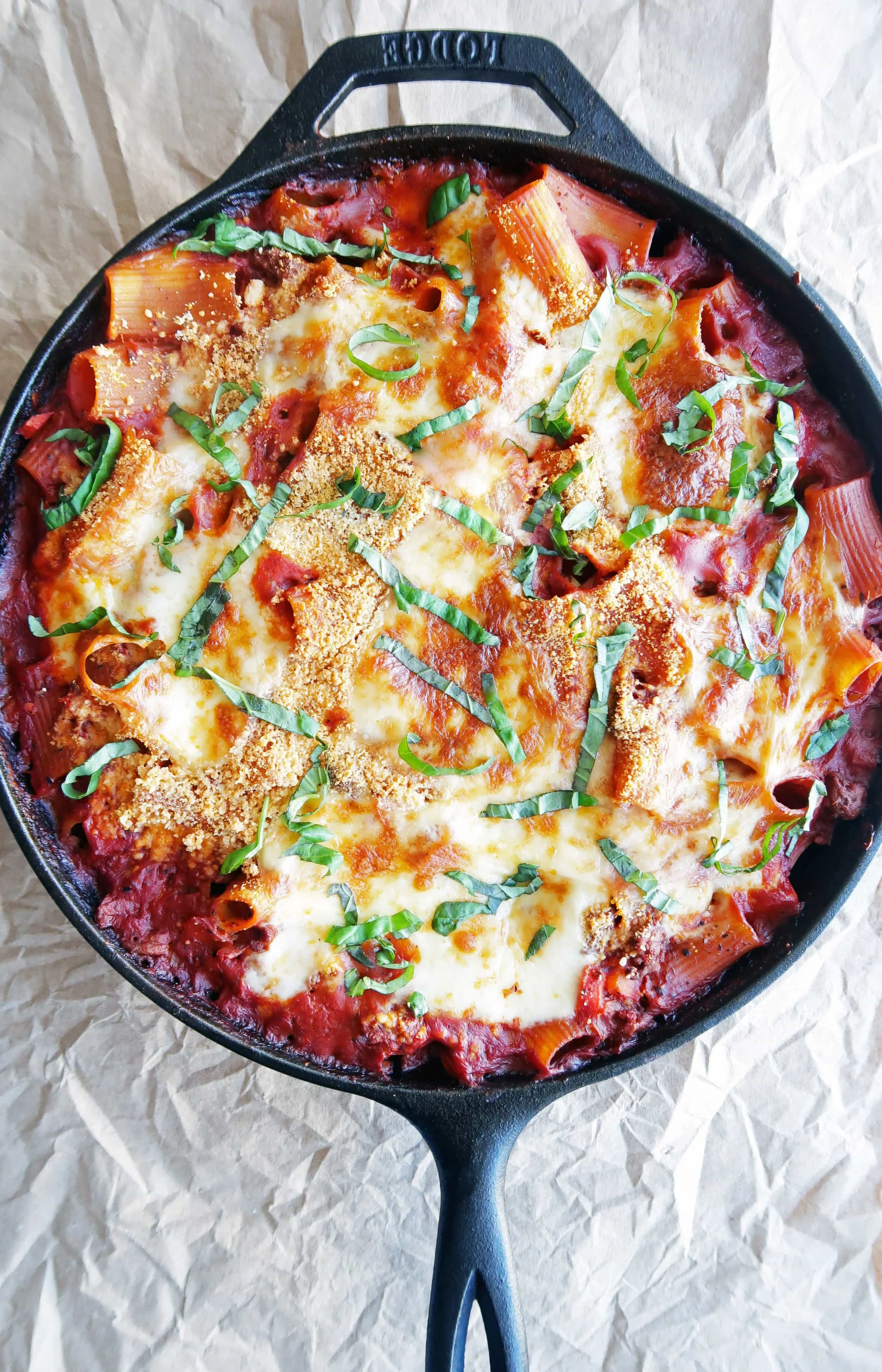 Baked Beef Pasta Casserole with melted cheesy topping and fresh basil in a cast-iron skillet.