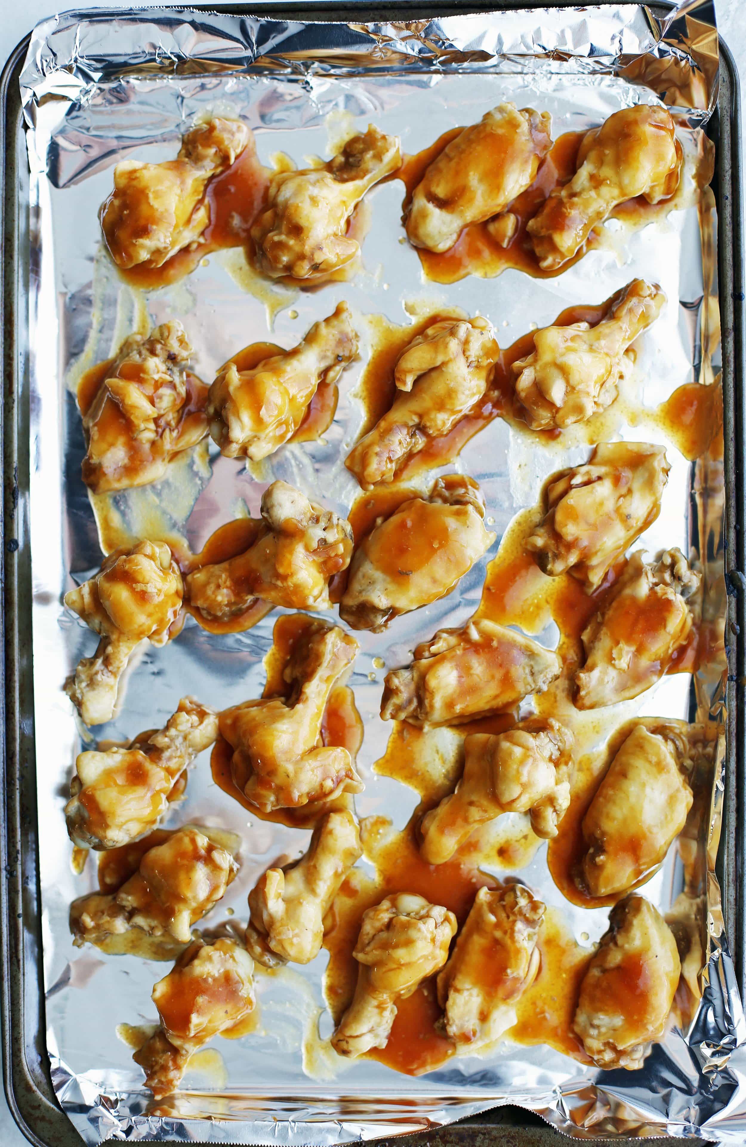 Cooked chicken wings coated with orange teriyaki sauce is placed on a baking sheet in a single layer.