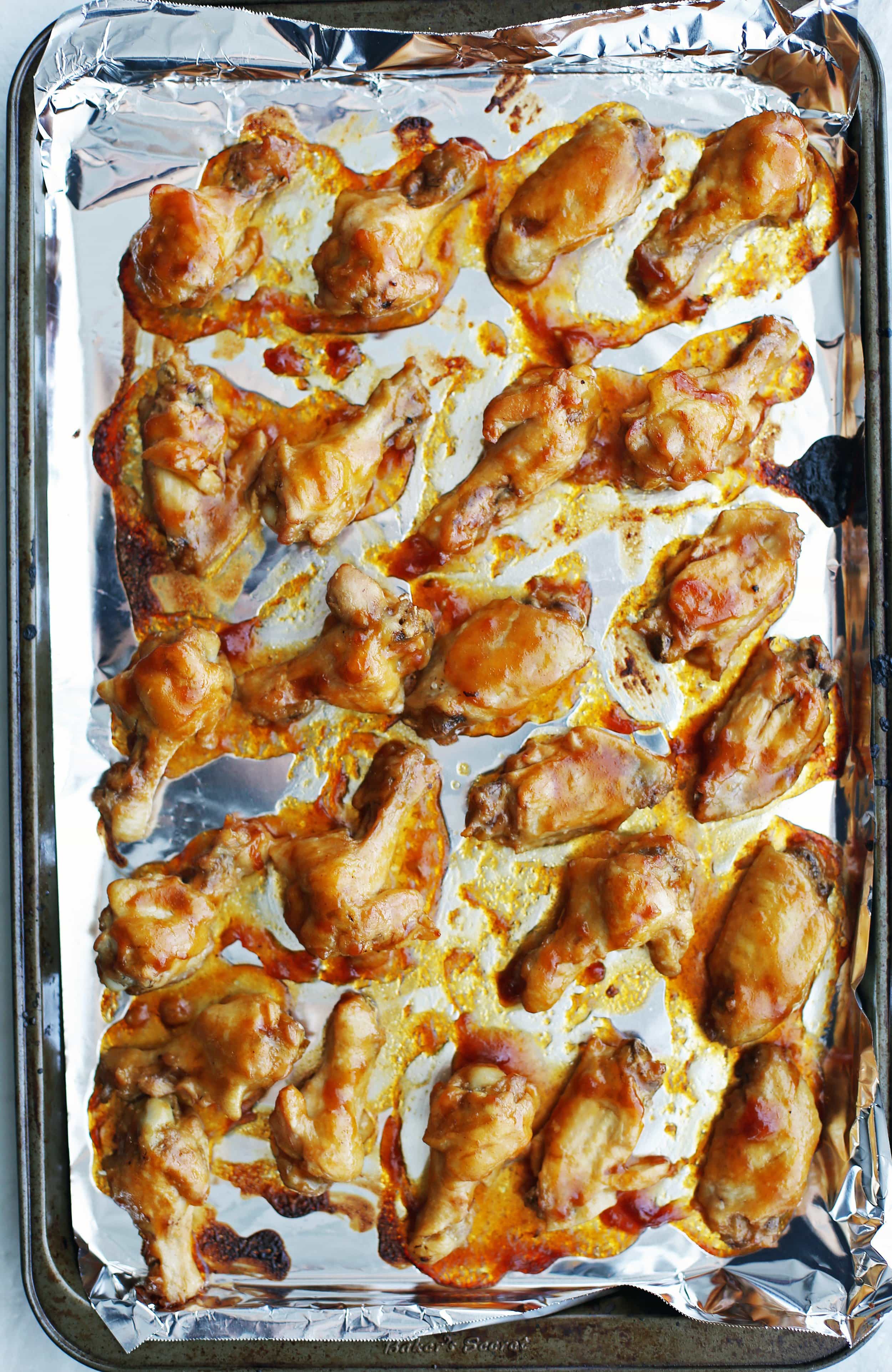 Shiny and sticky orange teriyaki chicken wings on a baking sheet just out of the oven.