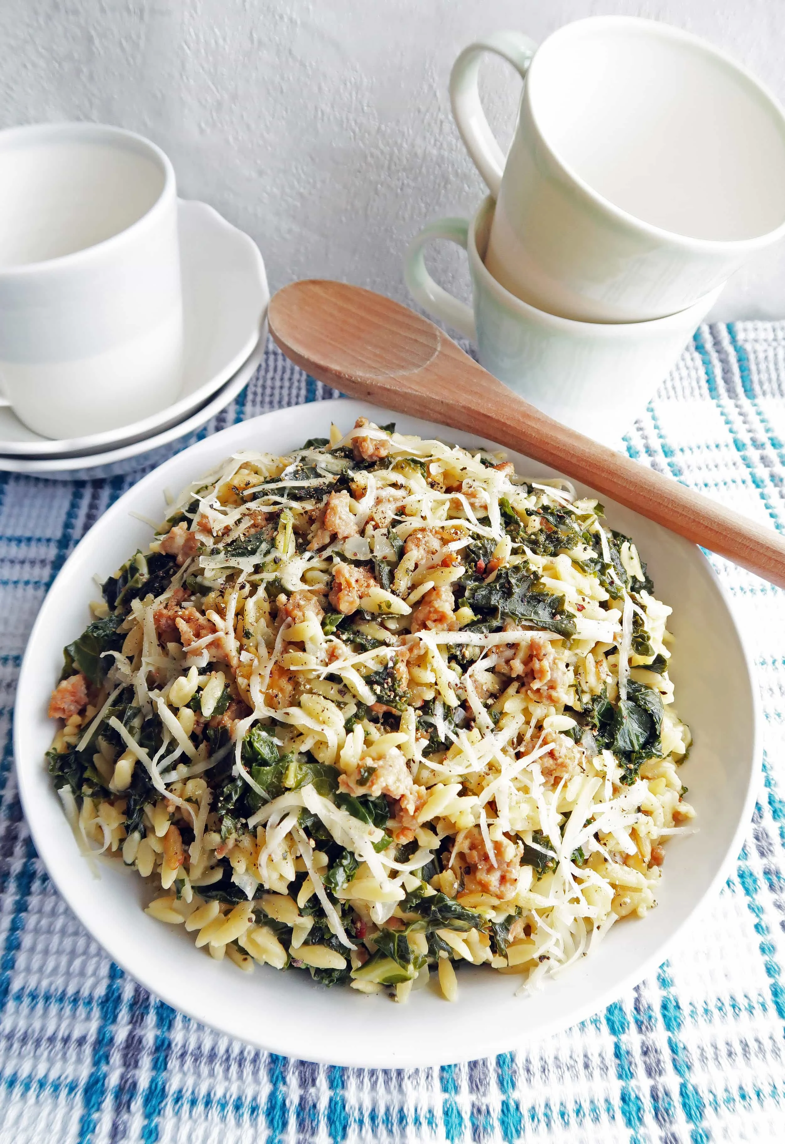 Orzo pasta with Italian sausage and kale with shredded cheese on top in a large pasta bowl.