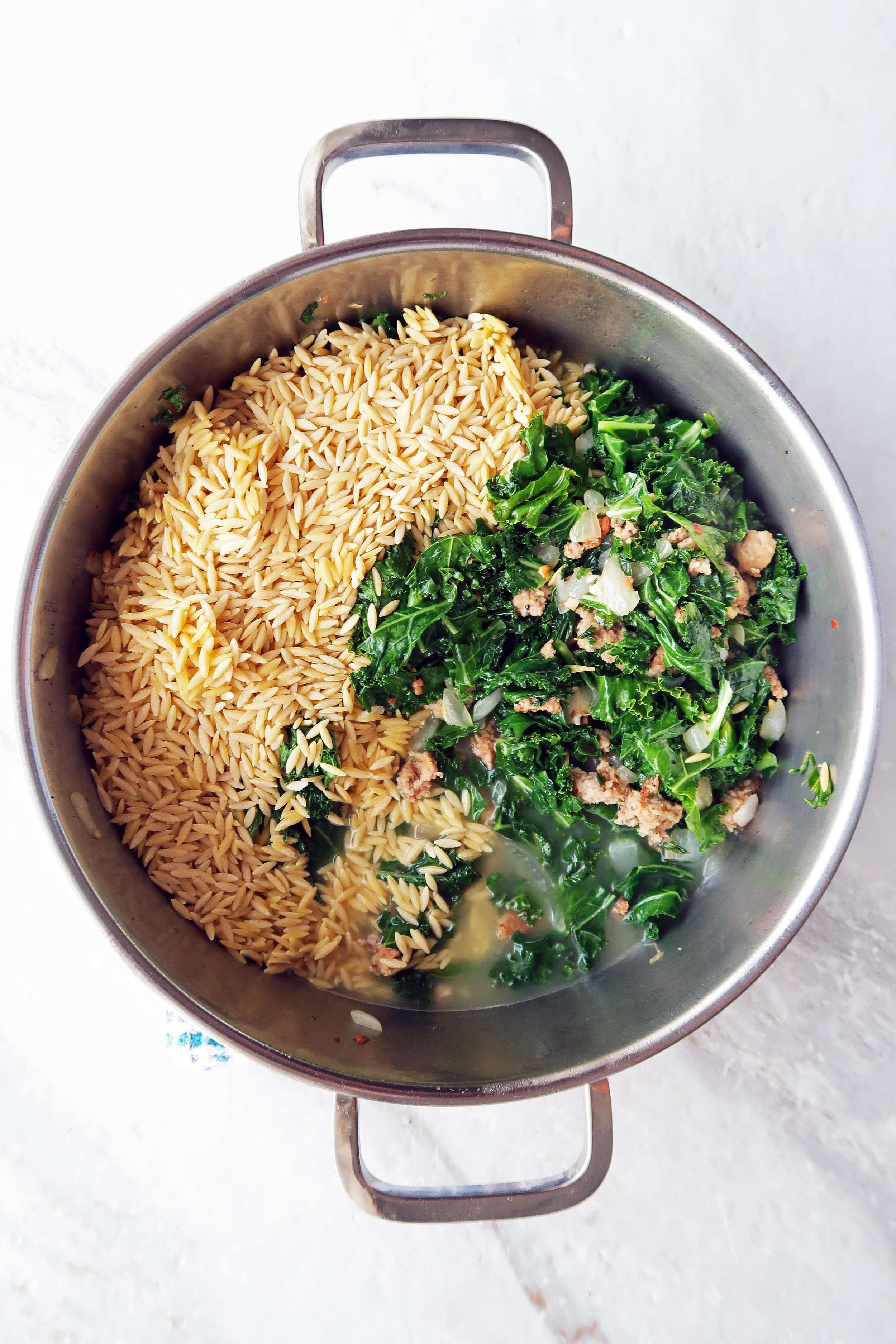 Cooked sausage, sautéed onion, garlic, and kale, broth, and uncooked orzo in a pot.