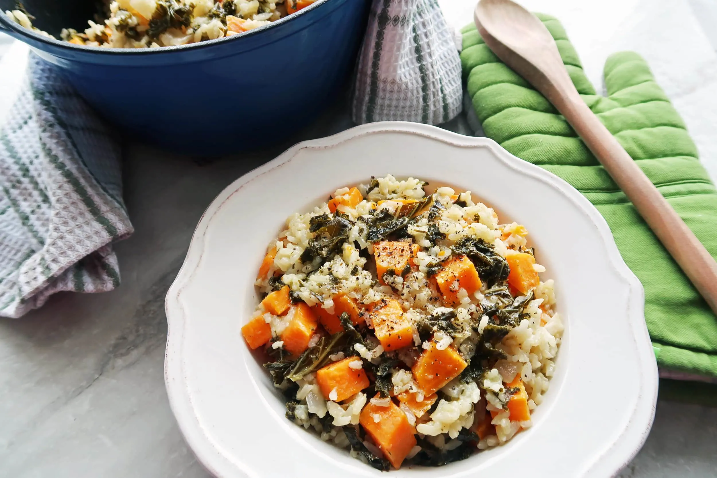 A Dutch oven and a white plate full of vegetarian, gluten-free sweet potato and kale risotto.