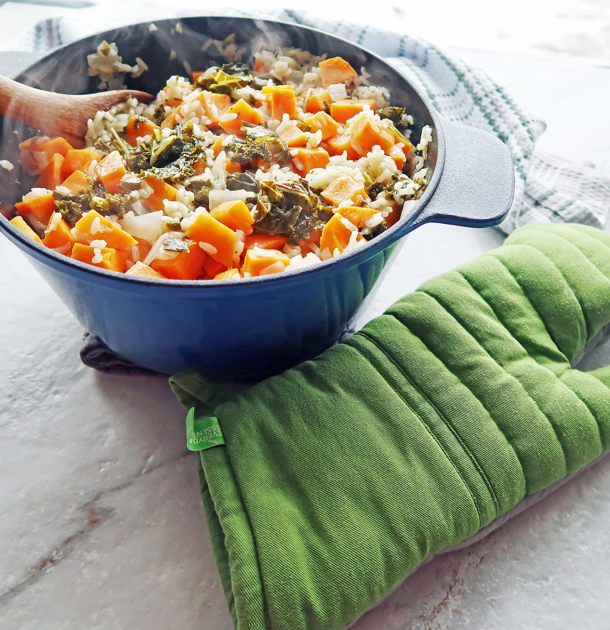 A Dutch oven full of vegetarian, gluten-free sweet potato and kale risotto with green oven mitt to its side.