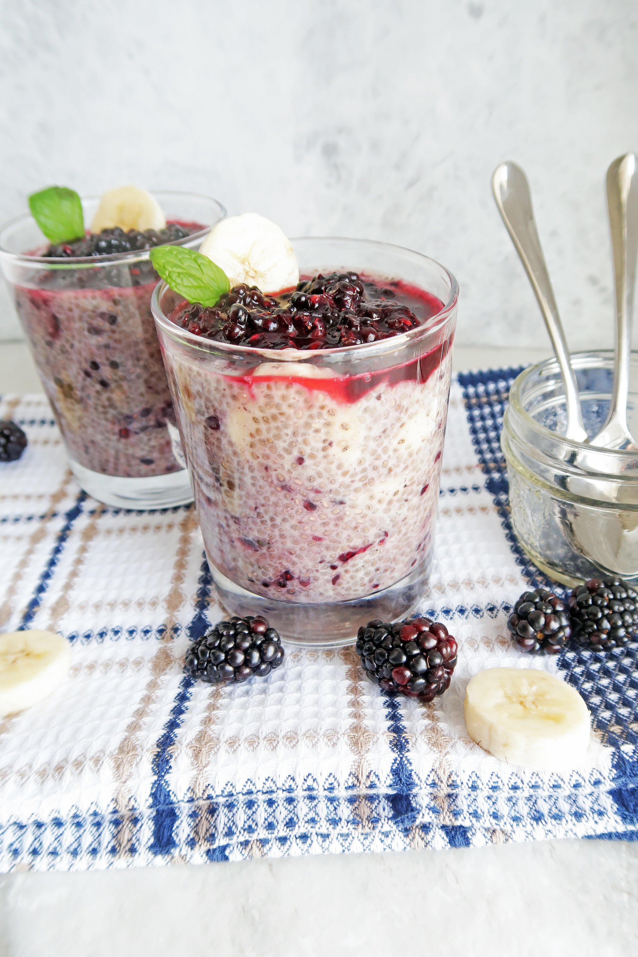 Overnight Chia Seed Pudding with Blackberries and Bananas in two glass tumblers with spoons, blackberries, and banana slices around them.