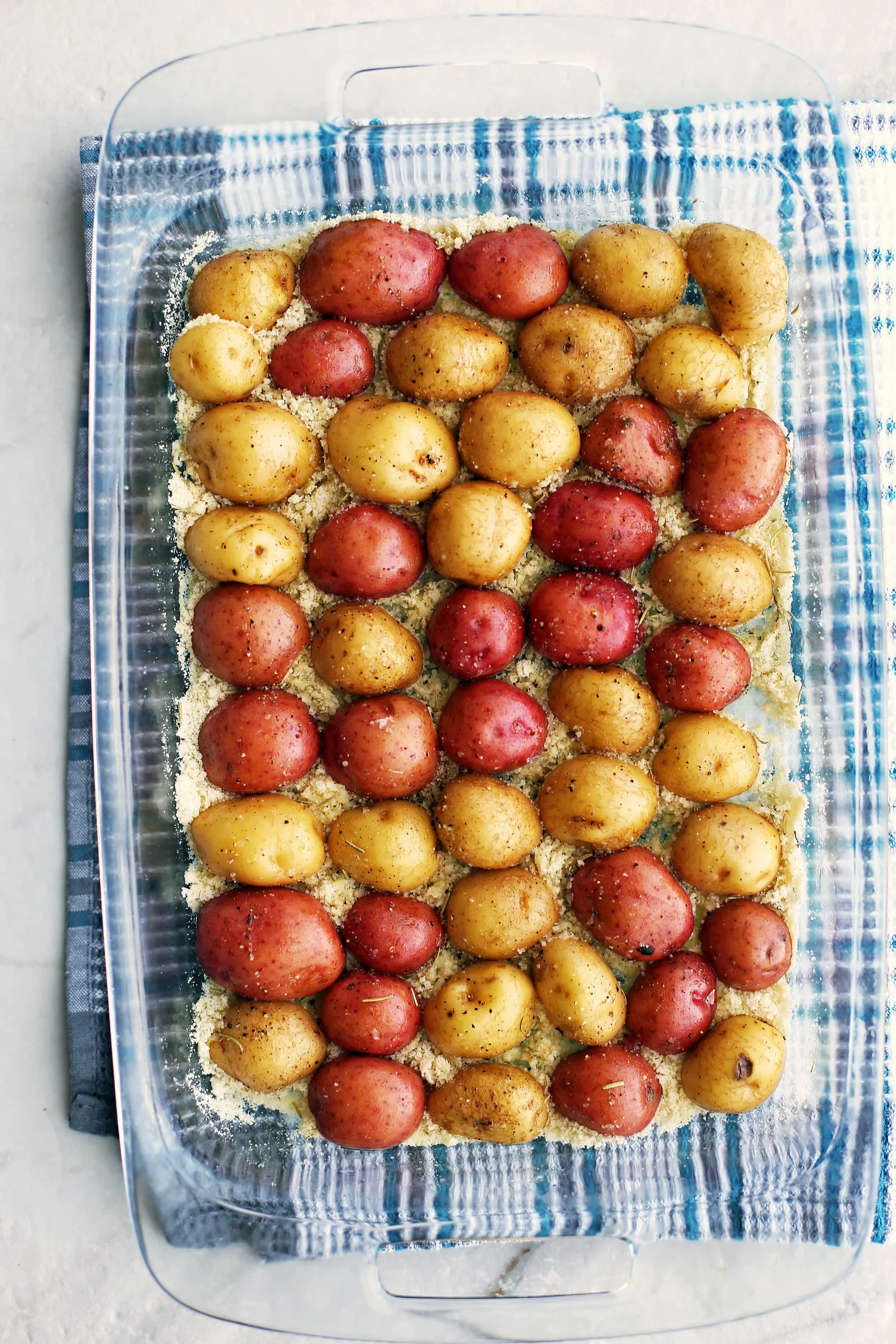 Halved baby potatoes placed cut side down, in a single layer, and pressed into a parmesan cheese mixture in a glass casserole dish that's ready to be baked.