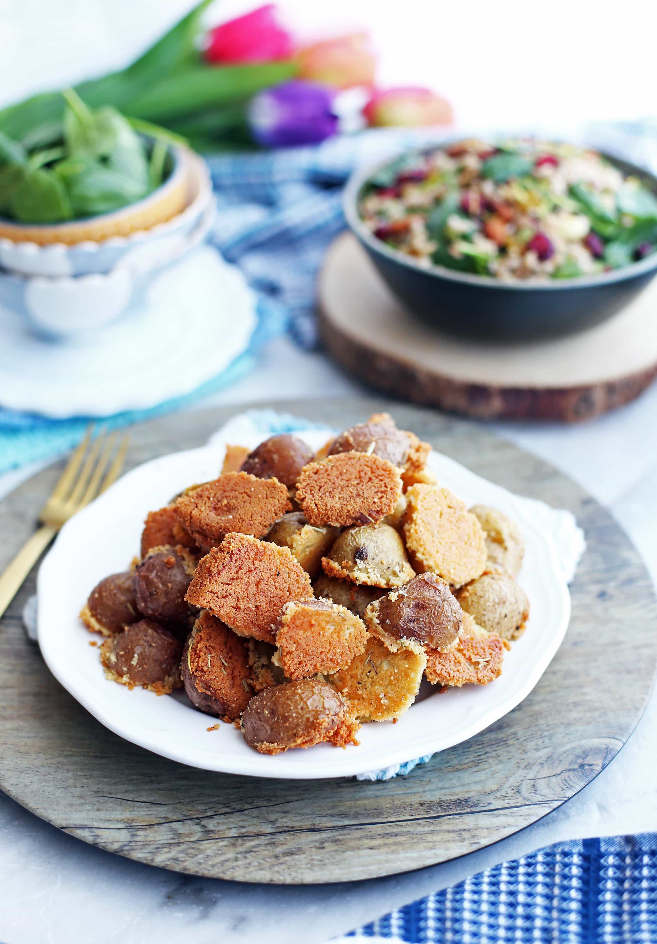 Crispy Parmesan Crusted Baby Potatoes piled on a white plate; a salad in a bowl behind it.