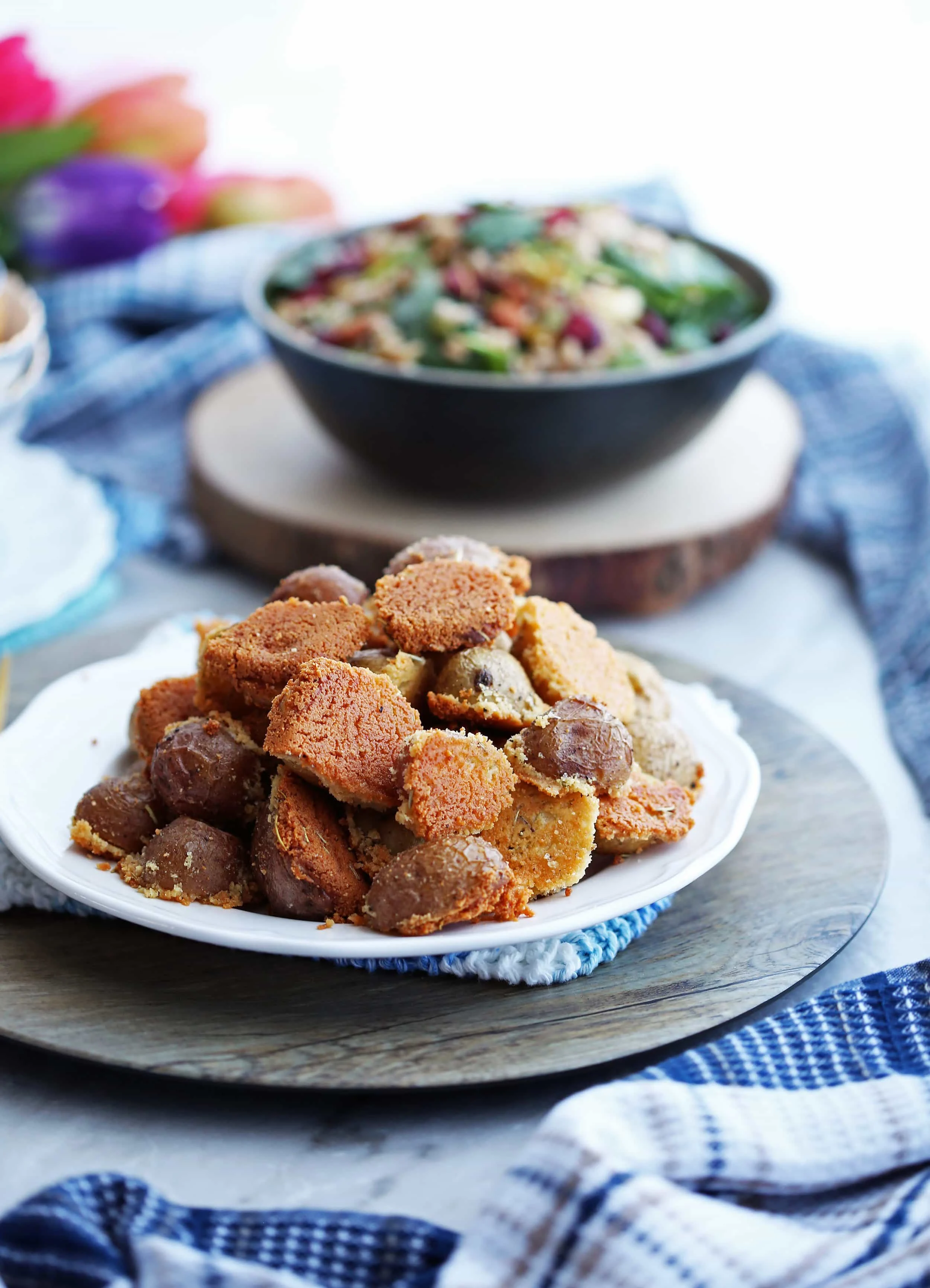 Crispy Parmesan Crusted Baby Potatoes piled on a white plate; a salad in a bowl in the background.