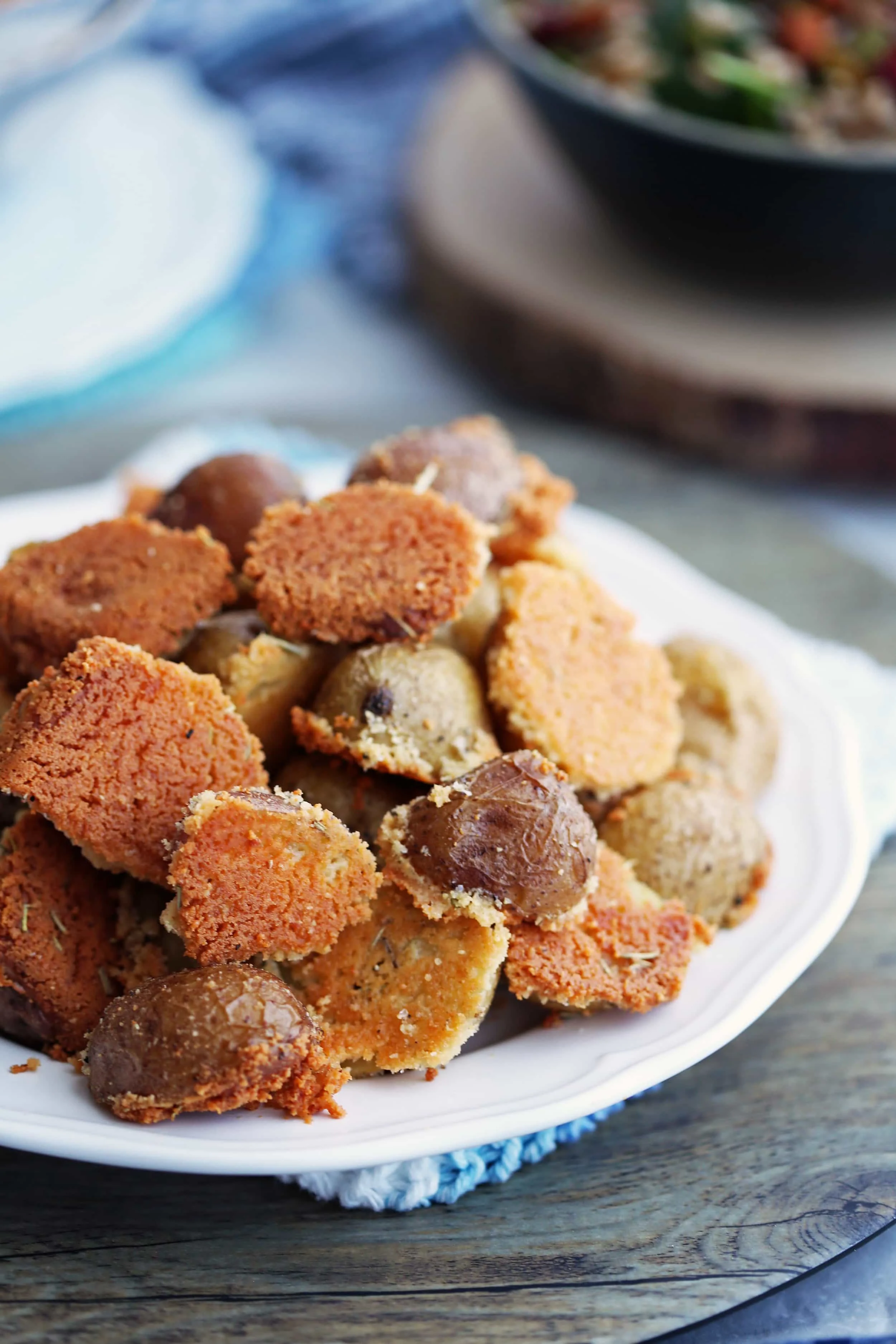 Close-up side view of Crispy Parmesan Crusted Baby Potatoes piled on a white plate.