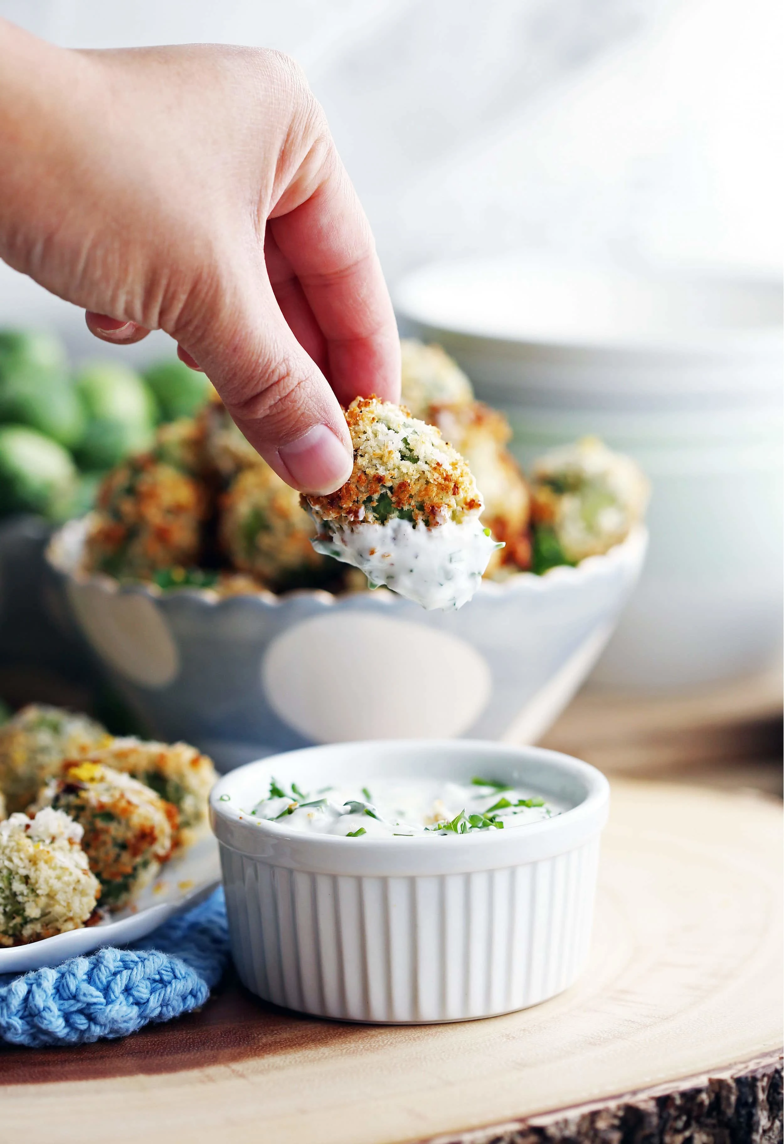 Fingers holding a single parmesan Panko Brussels sprout that has been dipped in sour cream sauce.