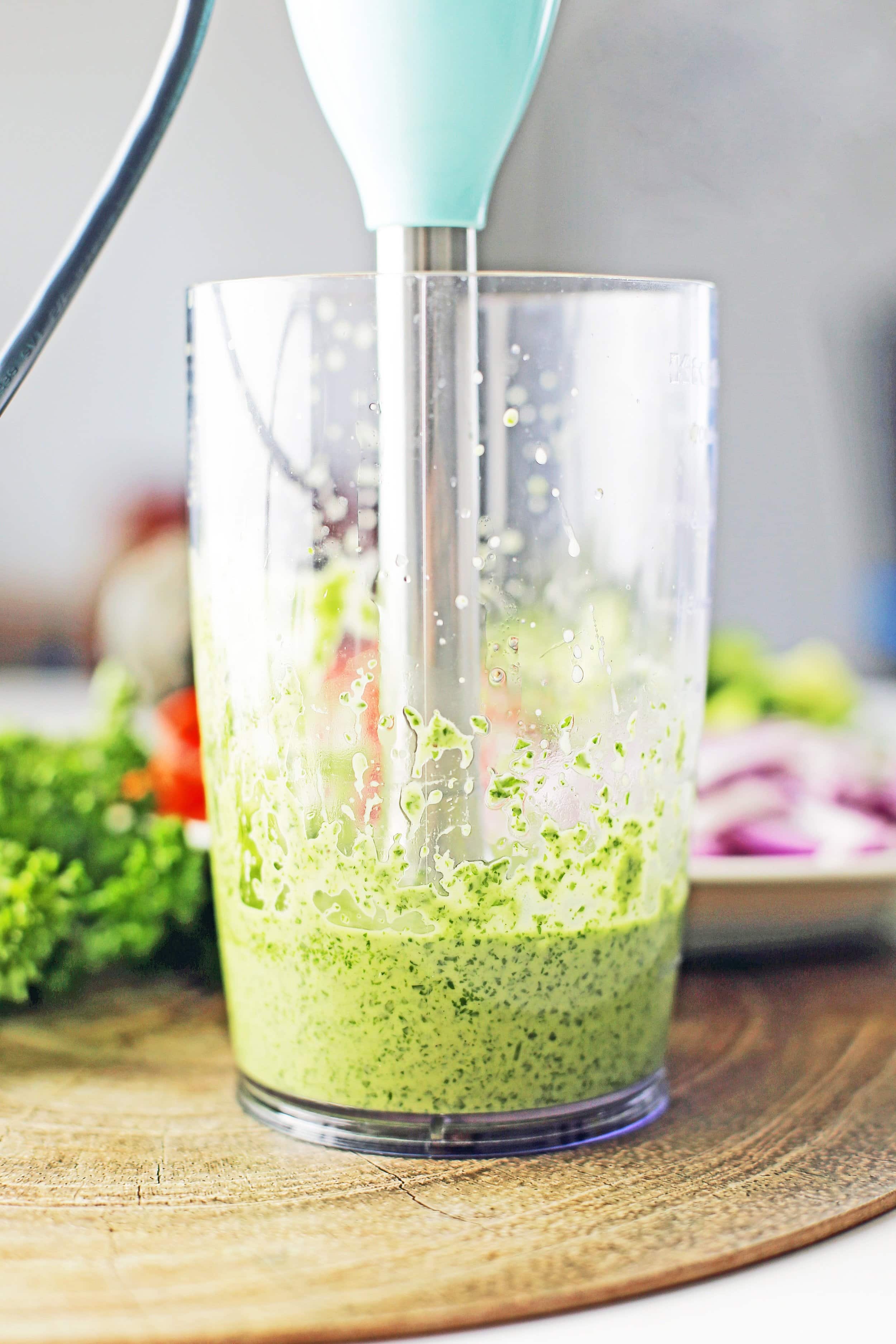 Green parsley dressing and immersion blender in a tall, clear plastic container.