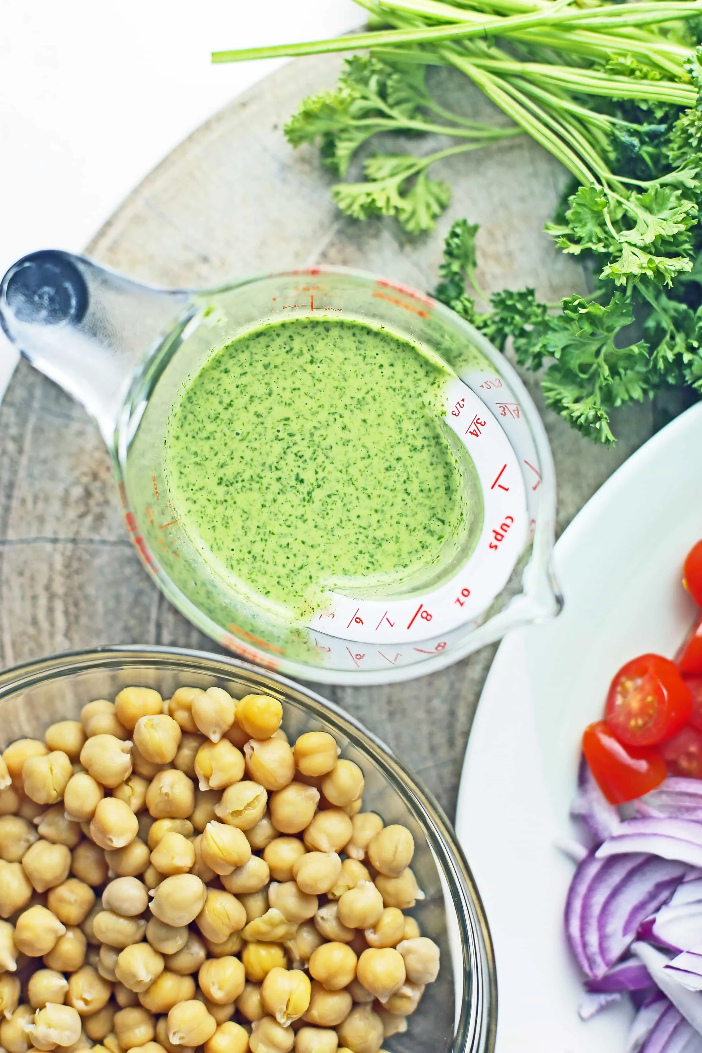 Overhead view of parsley dressing in a measuring cup and cooked chickpeas in a glass bowl.