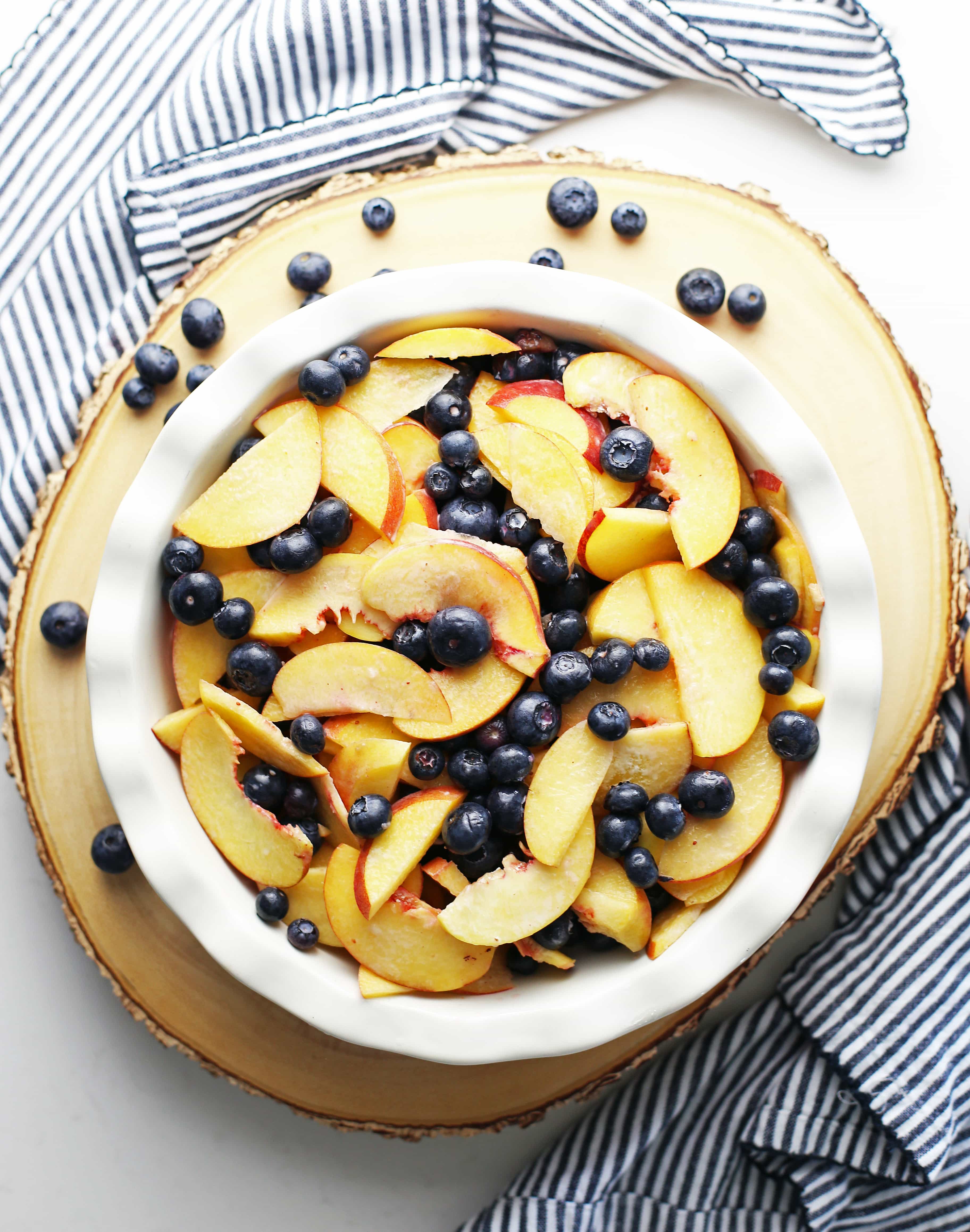 Overview view of a pie dish full of sliced peaches and blueberries tossed with sugar, lemon juice, and cornstarch.