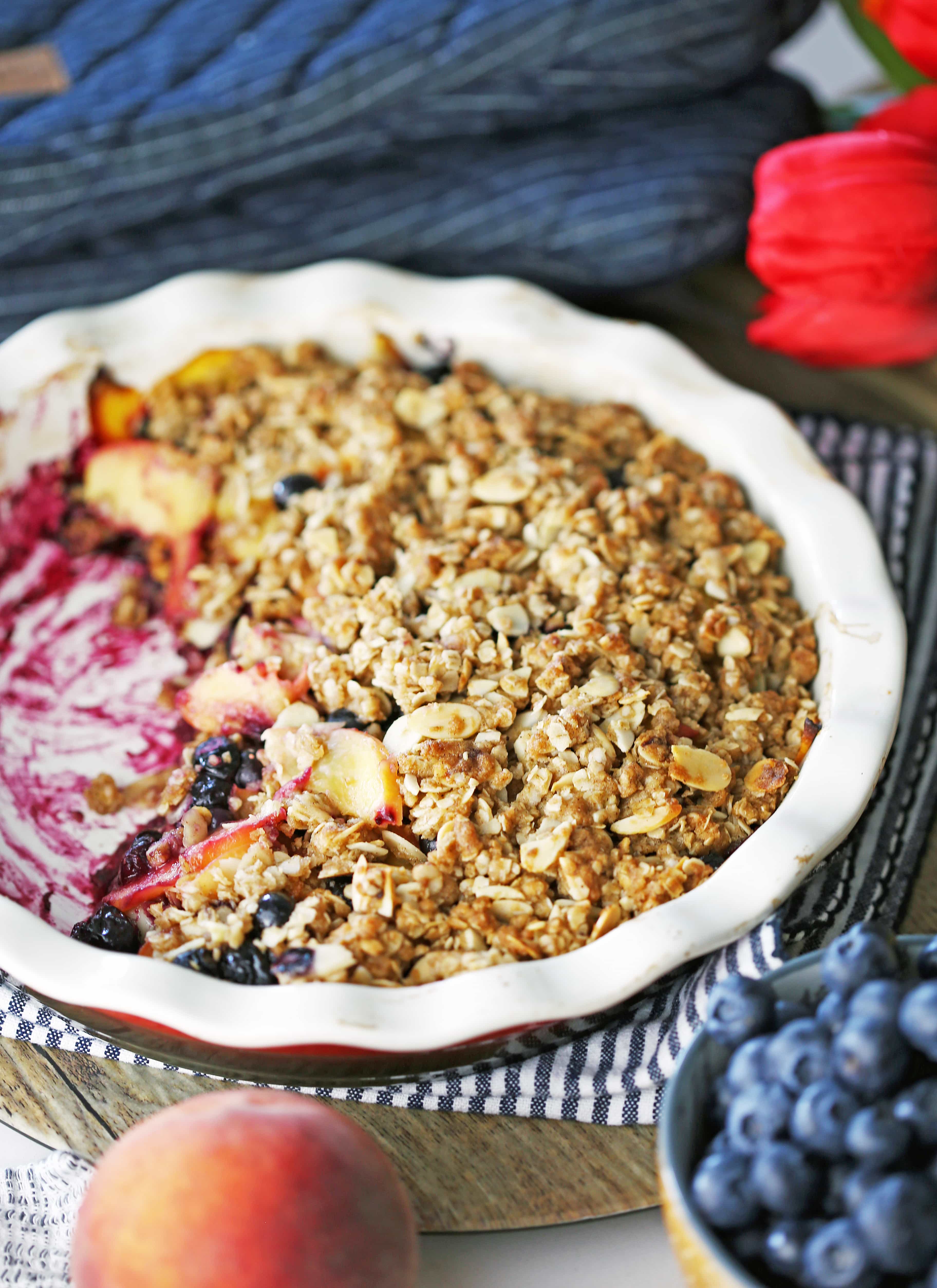 A white and red pie dish containing blueberry peach crisp with a scoop of crisp removed.