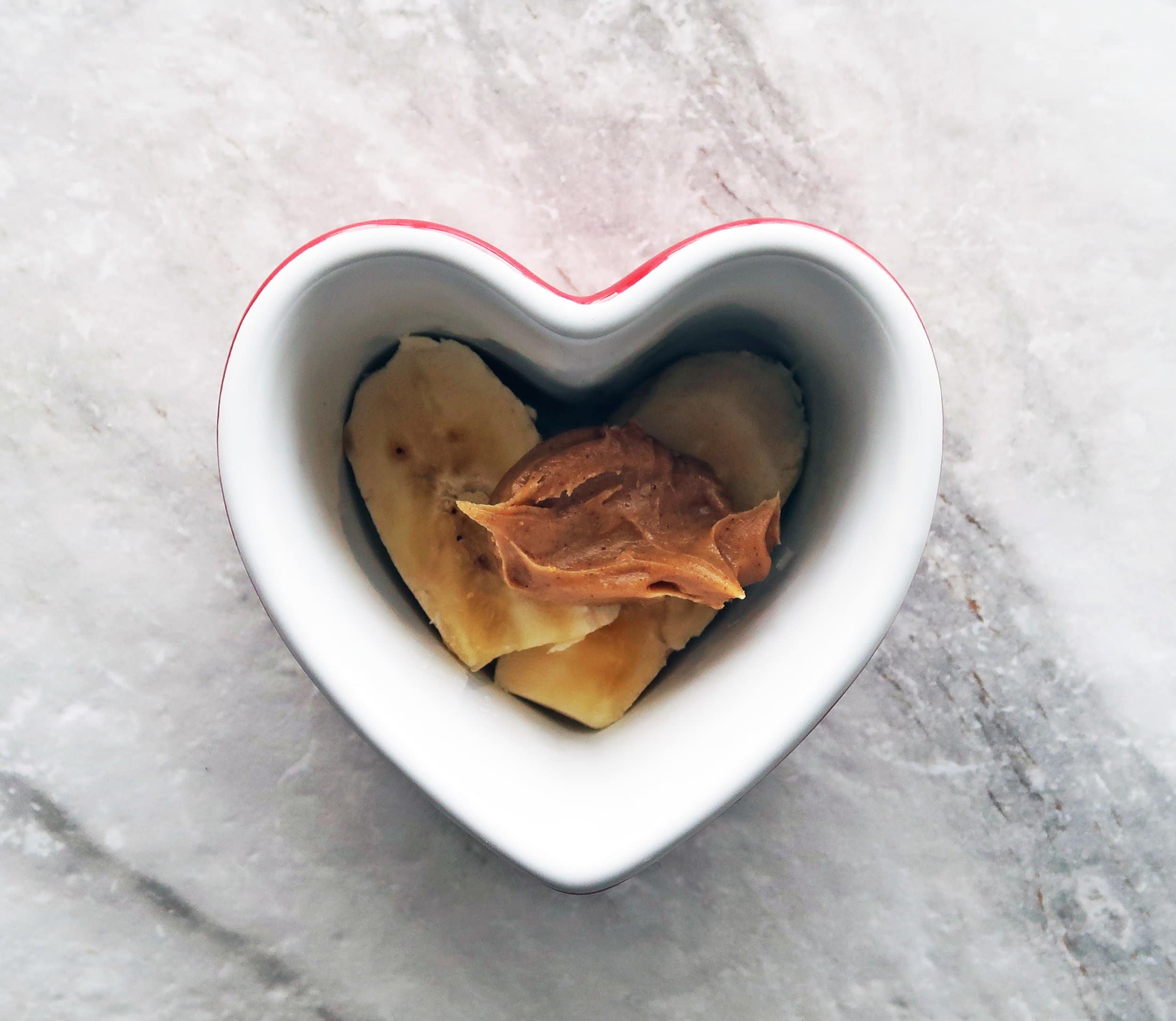 Bananas topped with peanut in a heart-shaped ramekin.