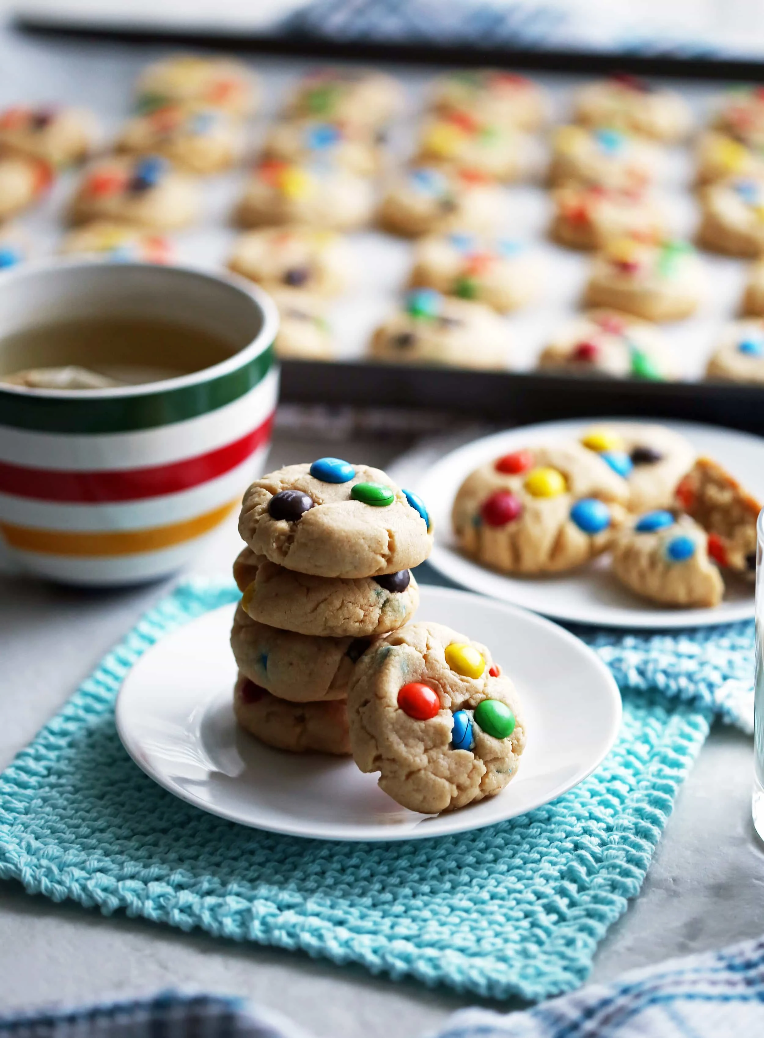 Side view of four staked peanut butter M&M's cookies with more cookies on a baking sheet in the background.