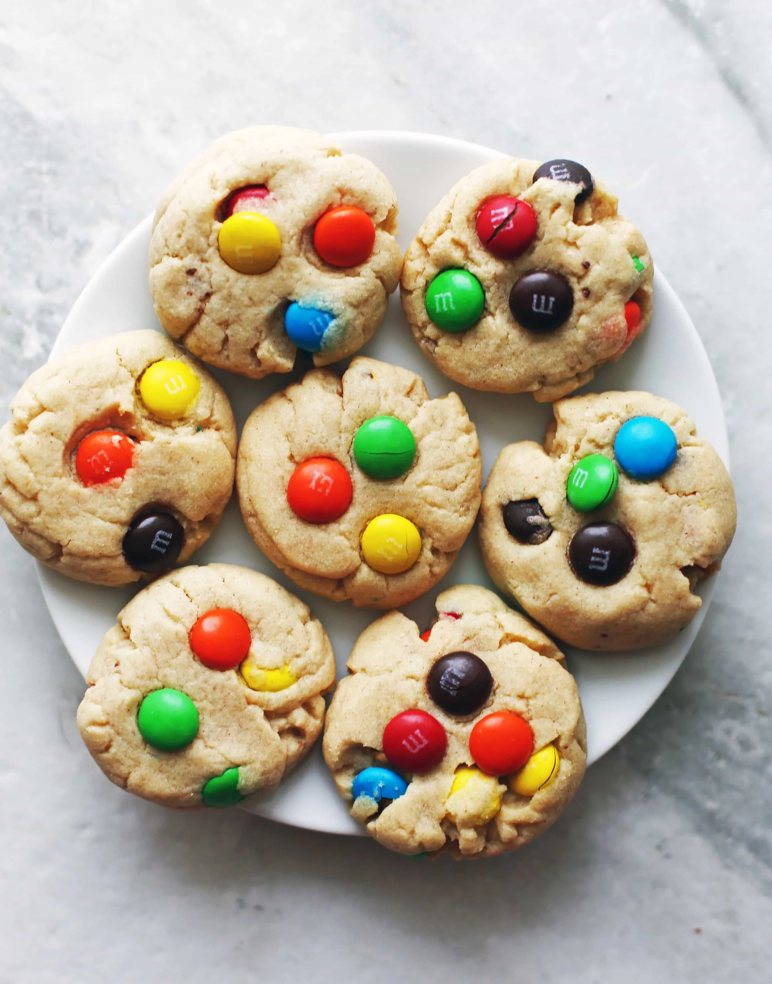 Overhead shot of seven Chewy Peanut Butter Cookies with Chocolate M&M's on a white plate.