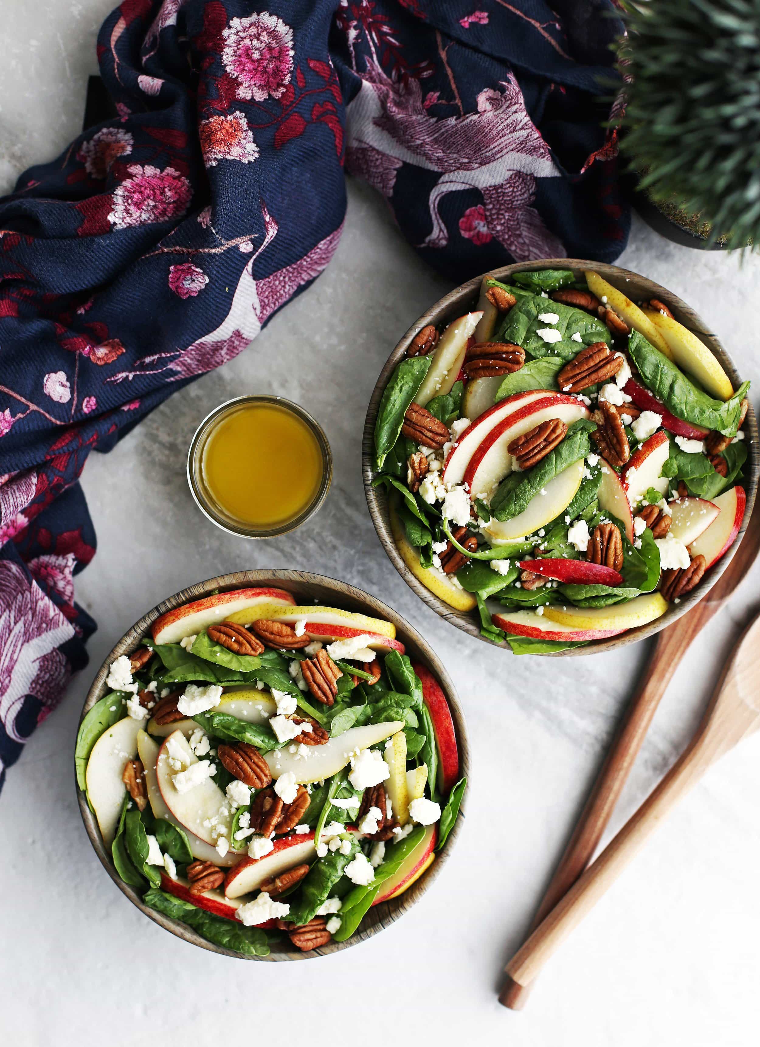 Overhead view of apple and pear spinach salad with pecans and feta cheese, vinaigrette to the side.