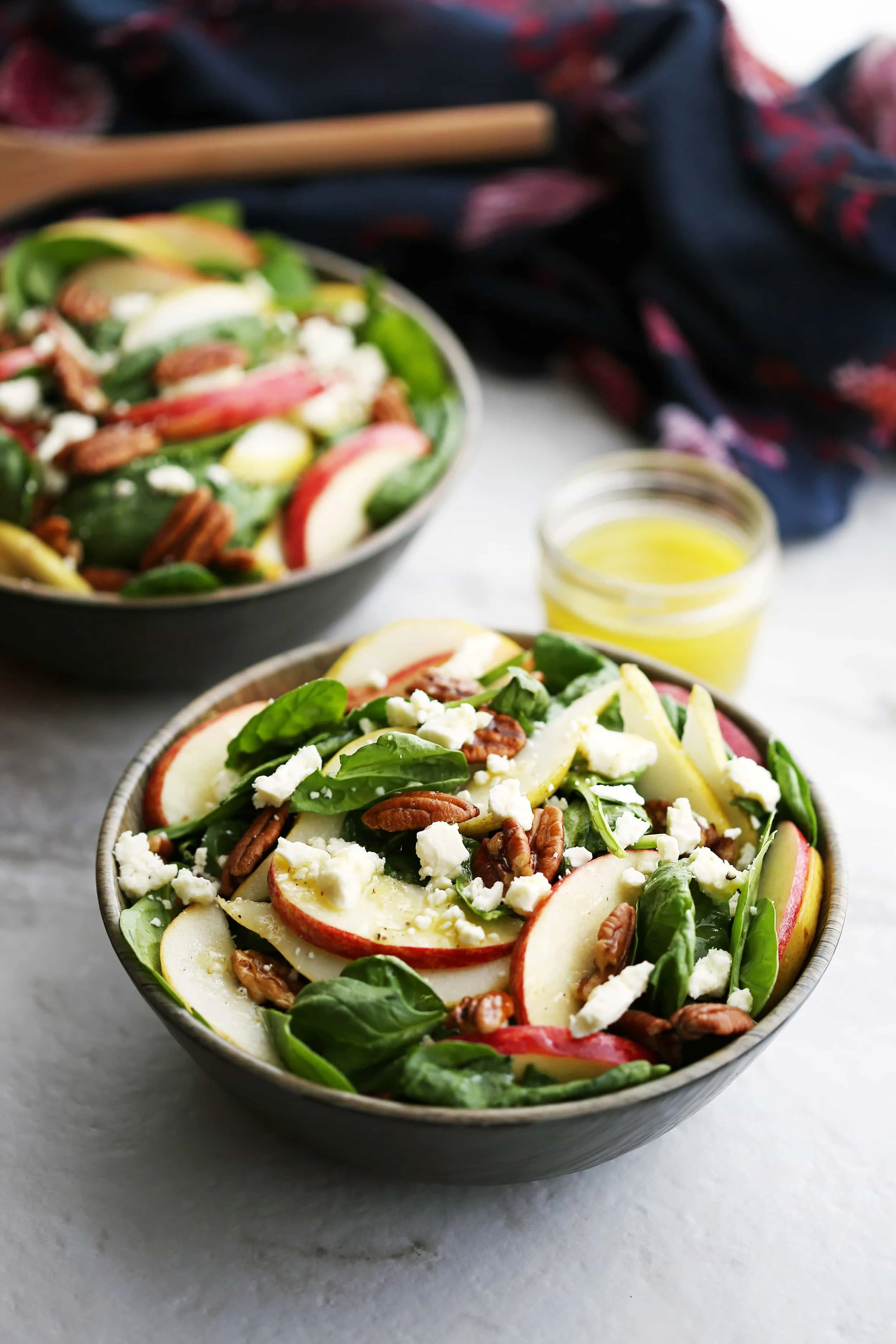 Top angled view of a bowl of apple and pear spinach salad with pecans and feta cheese.
