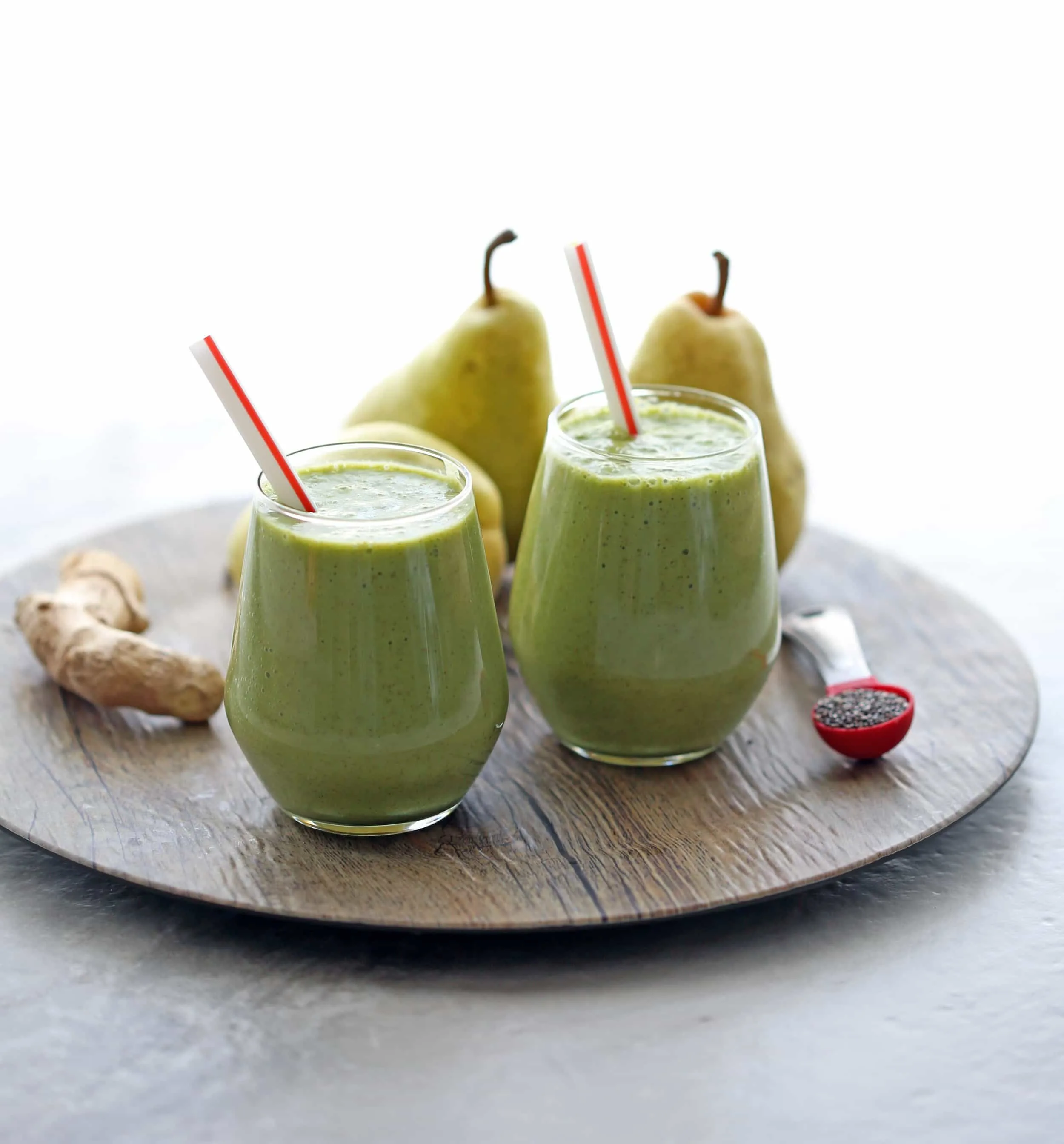 Two glasses of pear ginger chia smoothies with ginger root, pears, and chia seeds around it.