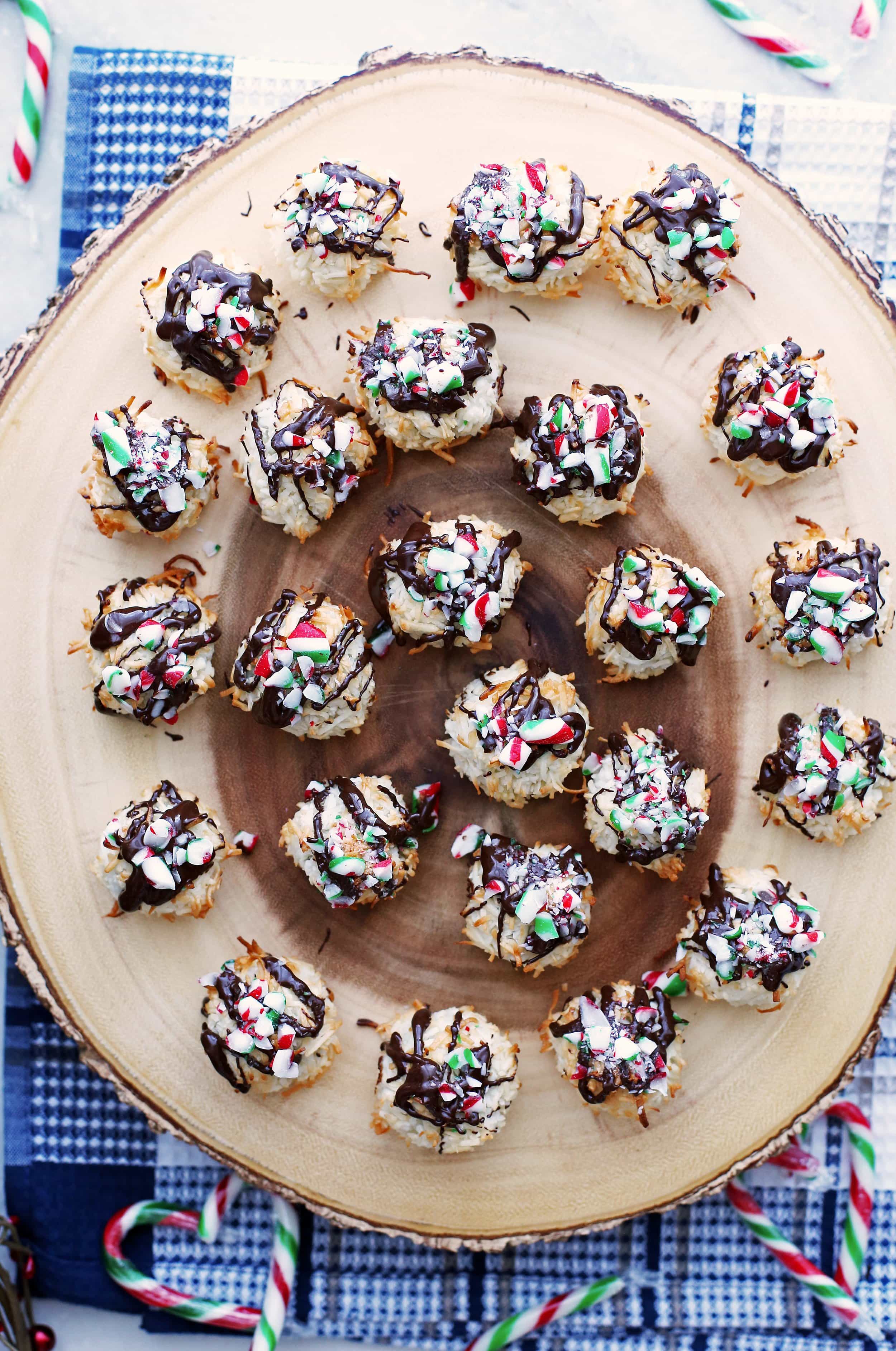 Coconut macaroons topped with melted chocolate and crushed candy canes on a wooden platter.