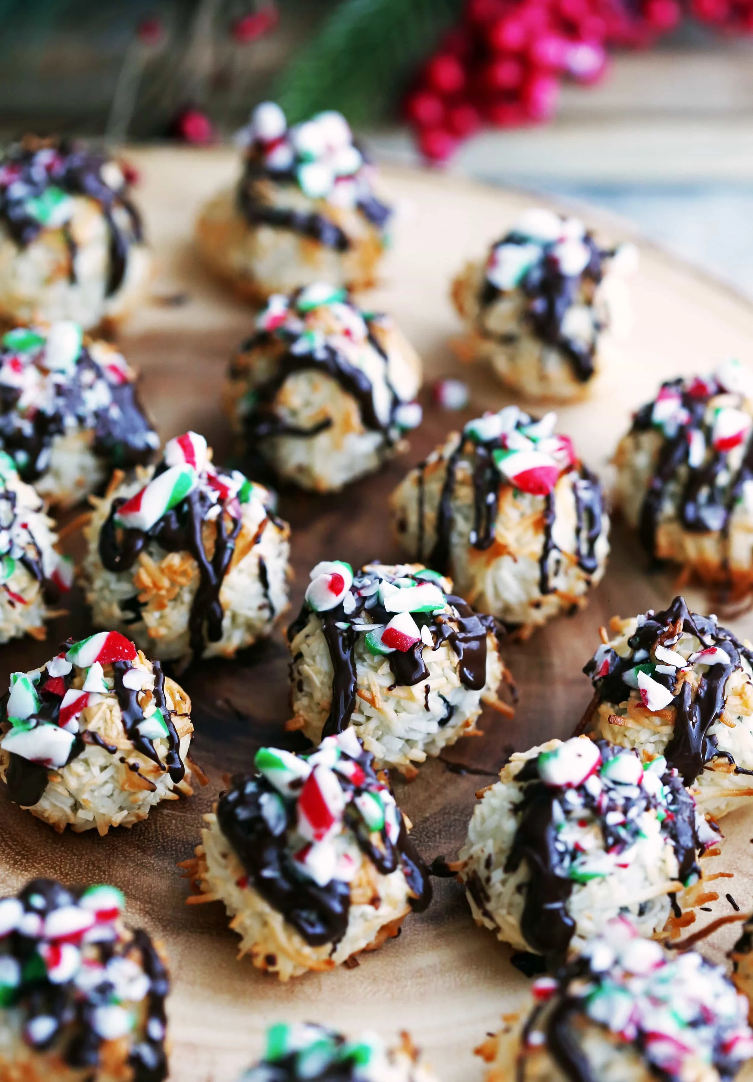 Many coconut macaroons topped with melted chocolate and crushed candy canes on a wooden platter.