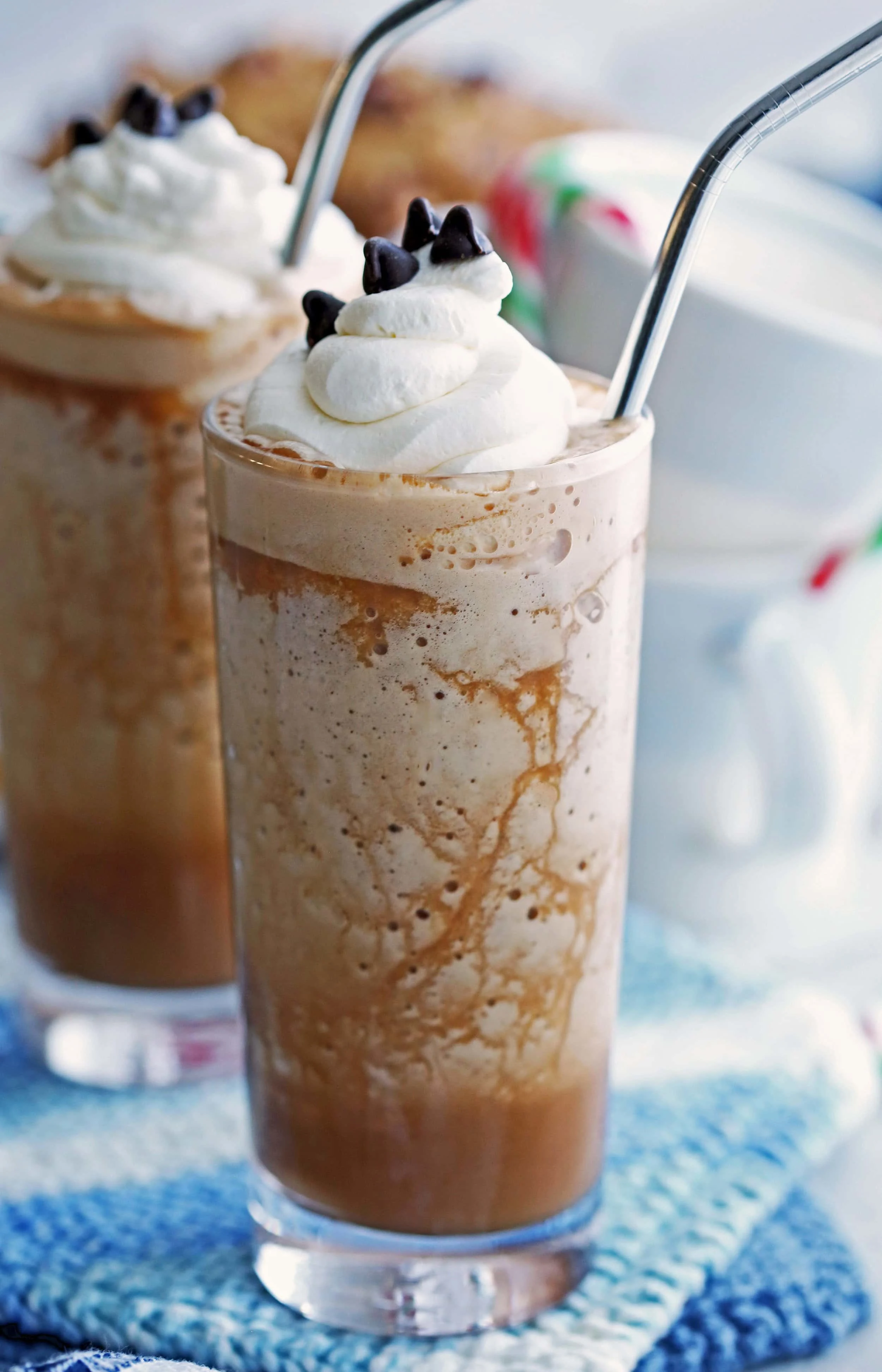 Peppermint mocha frappes topped with whipped cream and chocolate chips in two tall drinking glasses.