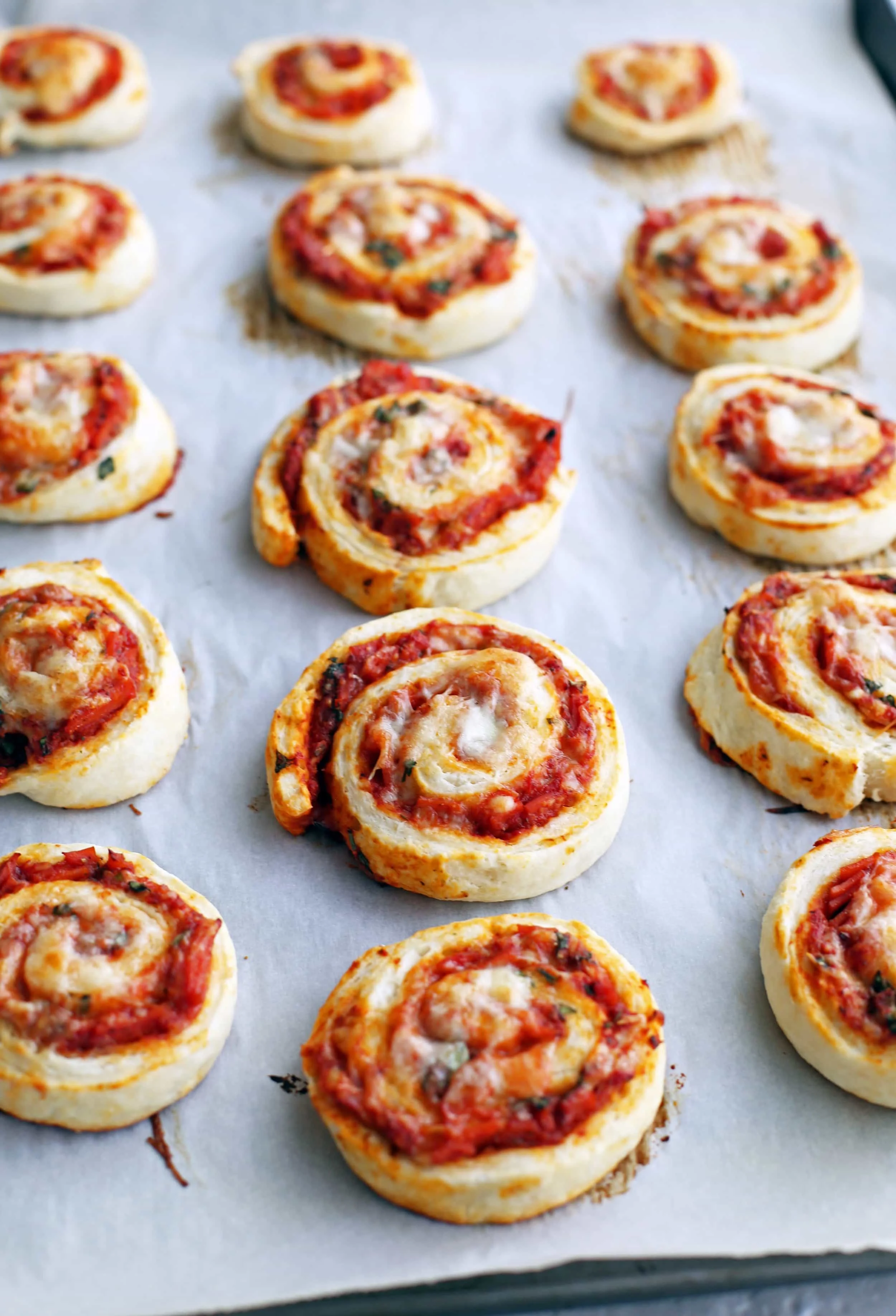 Freshly baked pepperoni cheese pizza rolls on a parchment paper lined baking sheet.